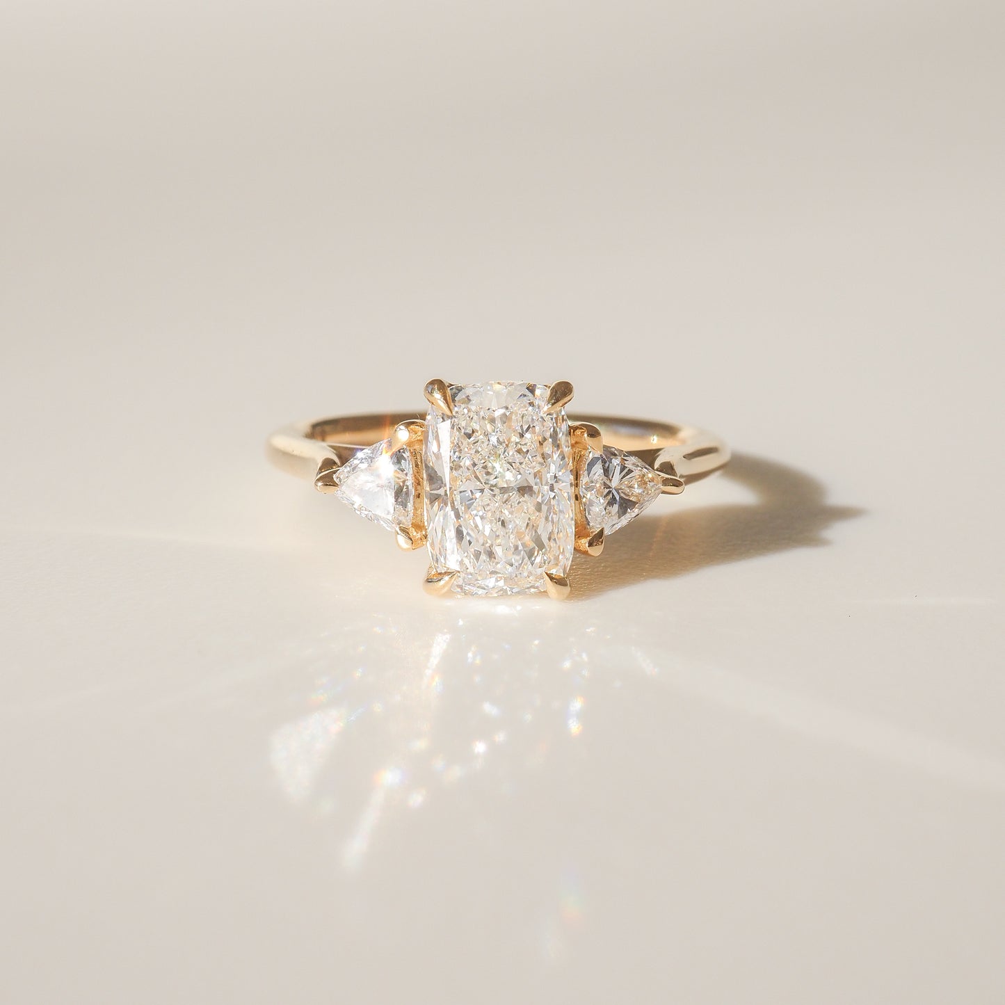 Gold trilogy ring with a radiant-cut centre diamond flanked by two triangular diamonds, set on a smooth band, reflecting light elegantly.