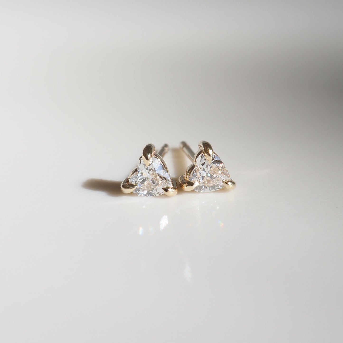 Trilliant-cut diamond stud earrings set in gold on a smooth, reflective surface. Luxurious, high-end jewellery.