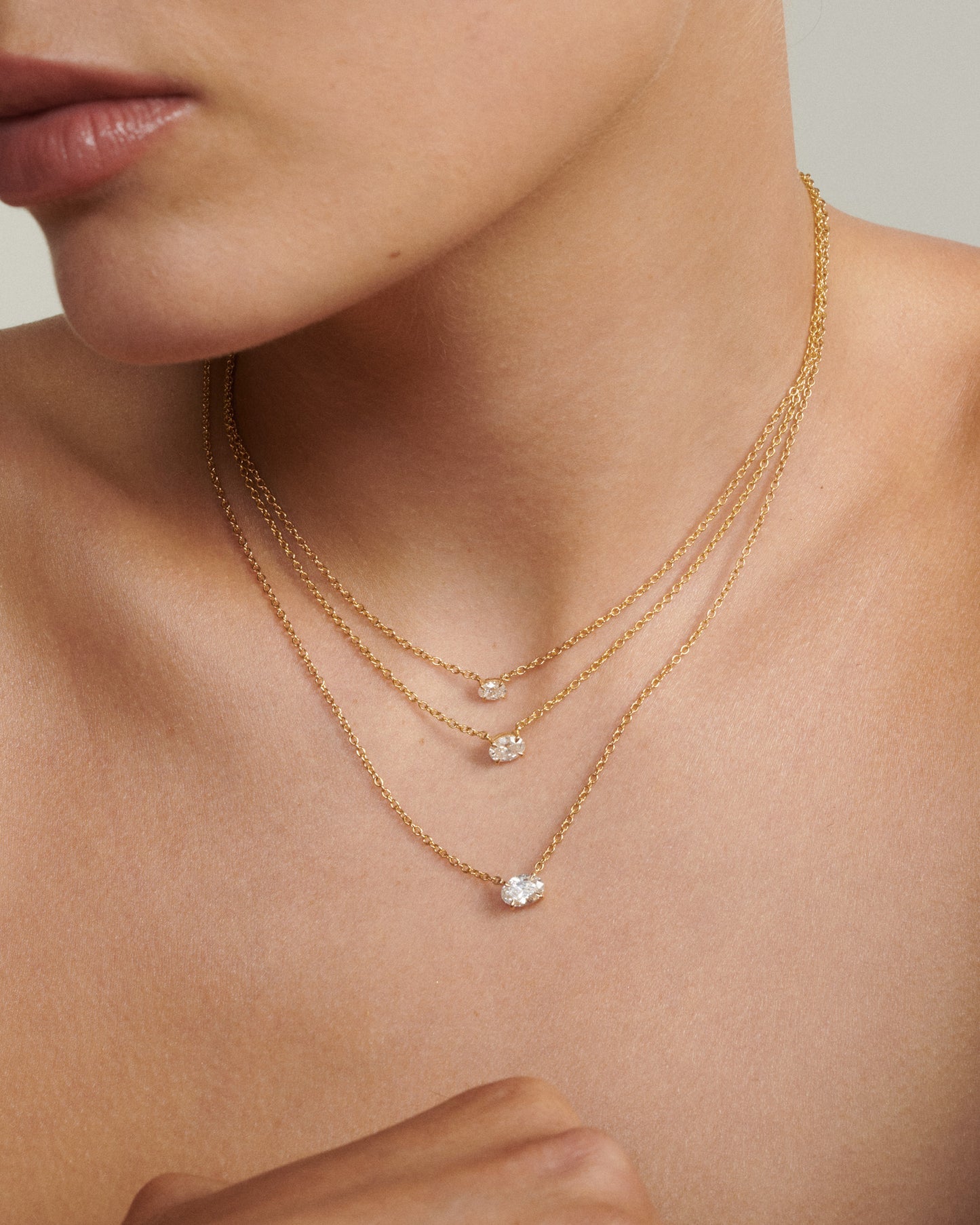 Close-up of a person wearing two gold necklaces with small pendants on a neutral background