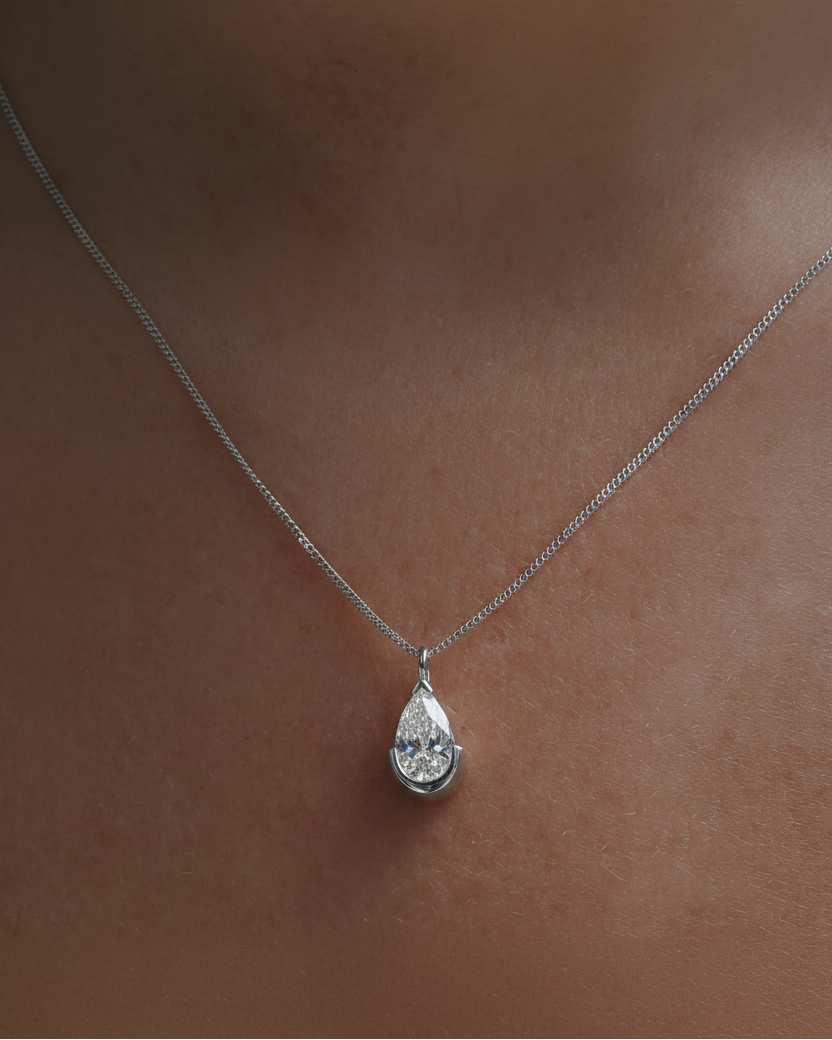 Gold necklace with a pear-shaped diamond pendant against skin, showcasing luxury jewellery.