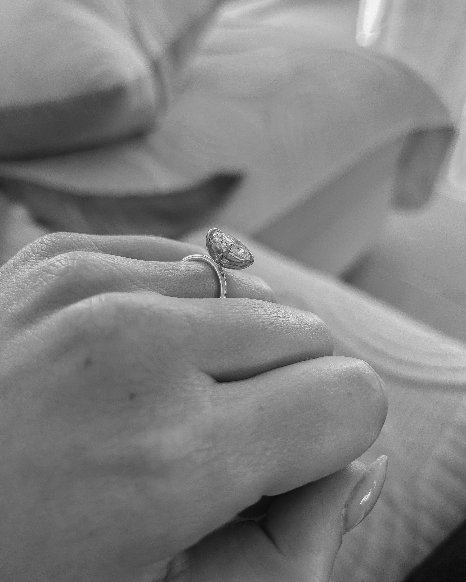 Close-up of a hand showcasing an elegant diamond engagement ring, with a soft-focus background of plush furnishings.