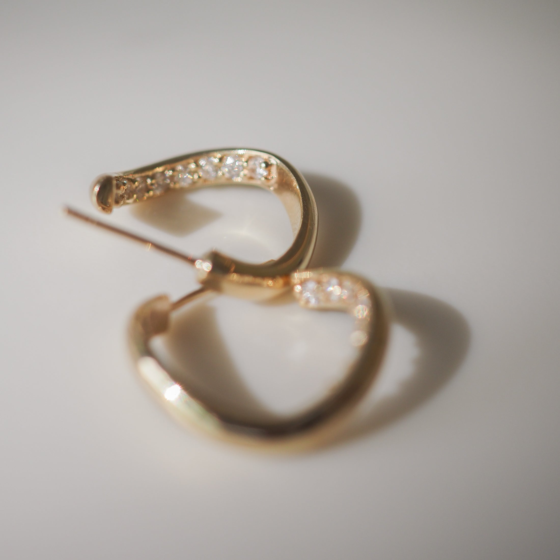 Elegant gold hoop earrings with inset diamonds, casting soft shadows on a light surface.