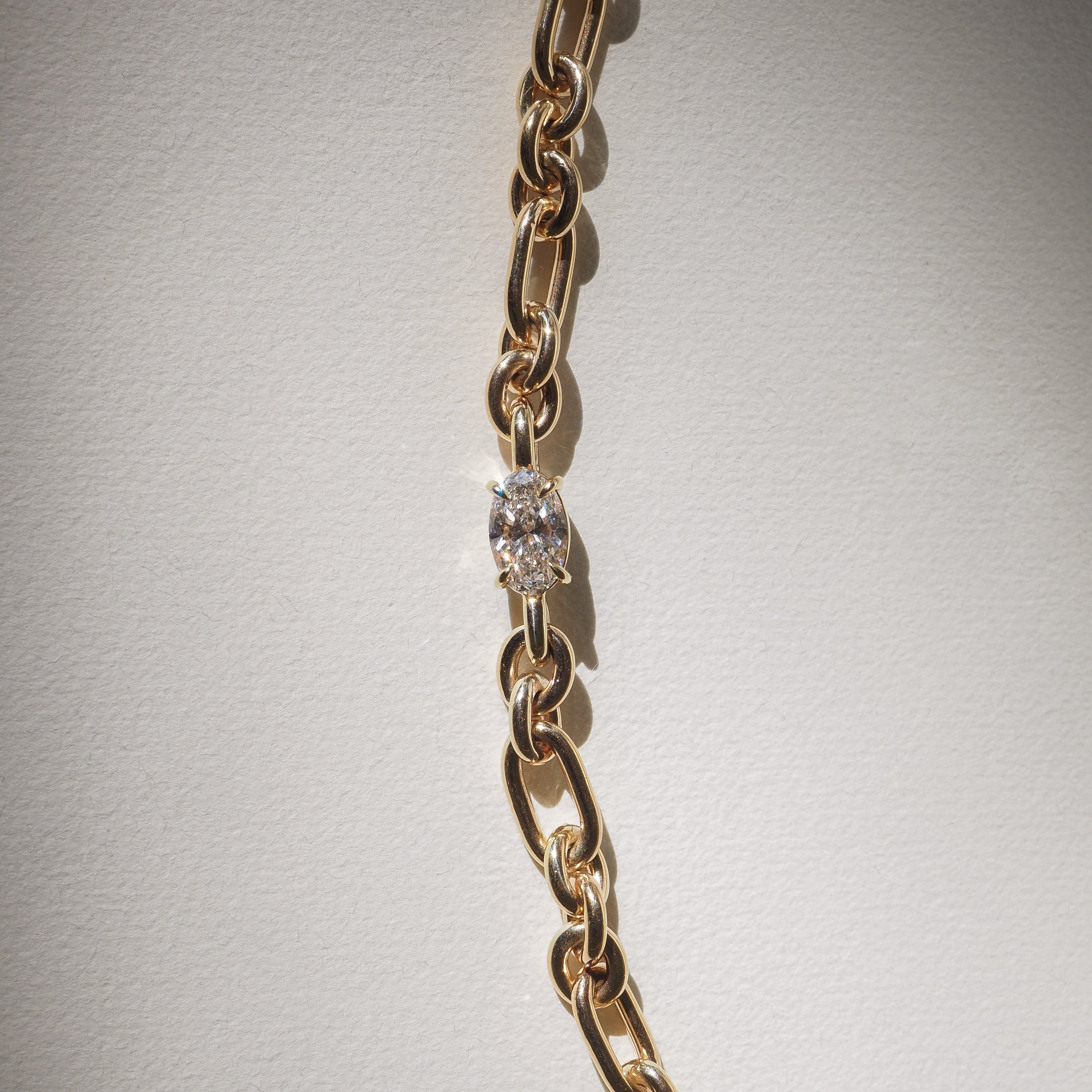 Gold chain link bracelet with a single sparkling diamond, elegantly displayed on a light background. Luxury jewellery detail.