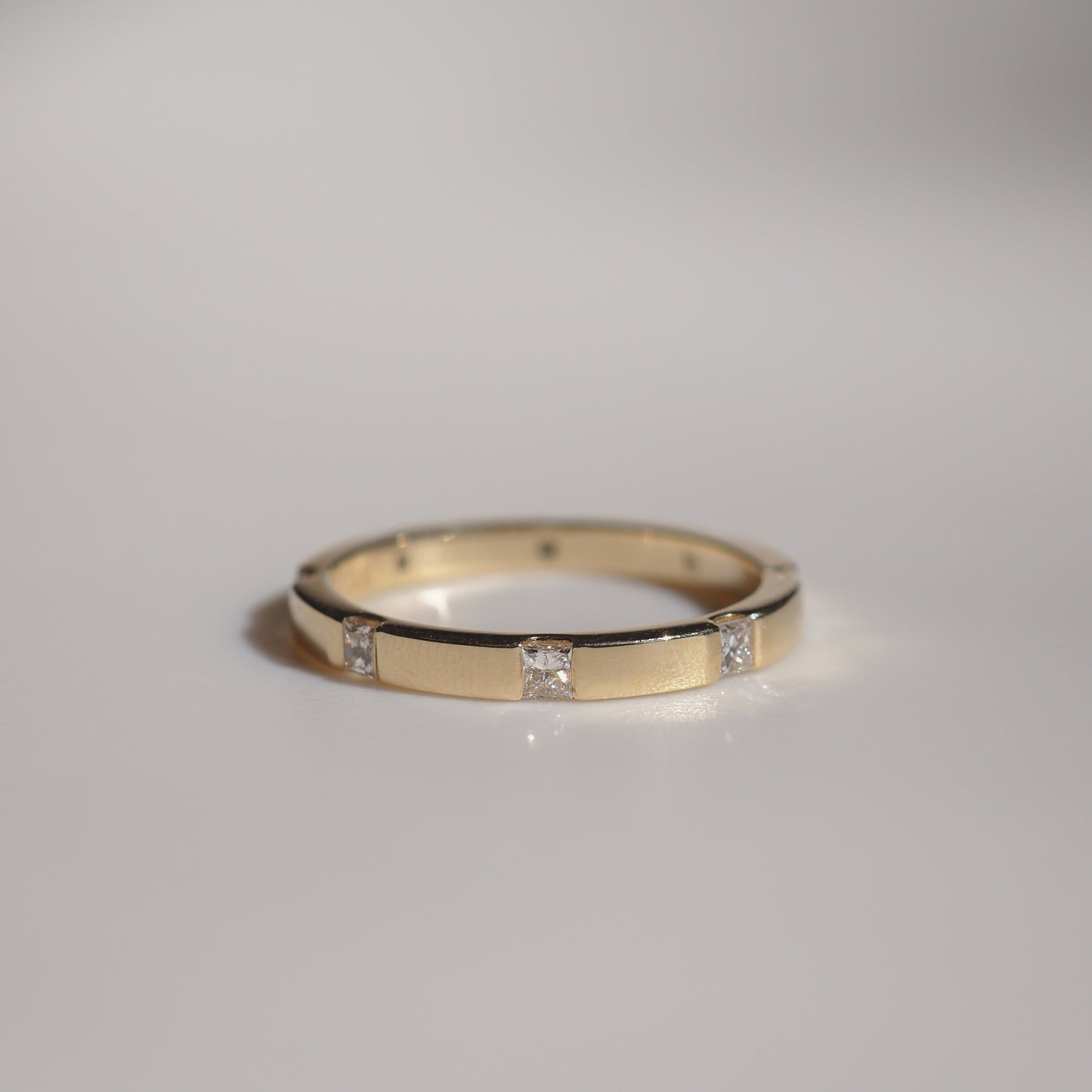 Elegant gold ring with evenly spaced diamond accents. Luxurious jewellery piece displayed on a soft grey surface, reflecting light subtly.