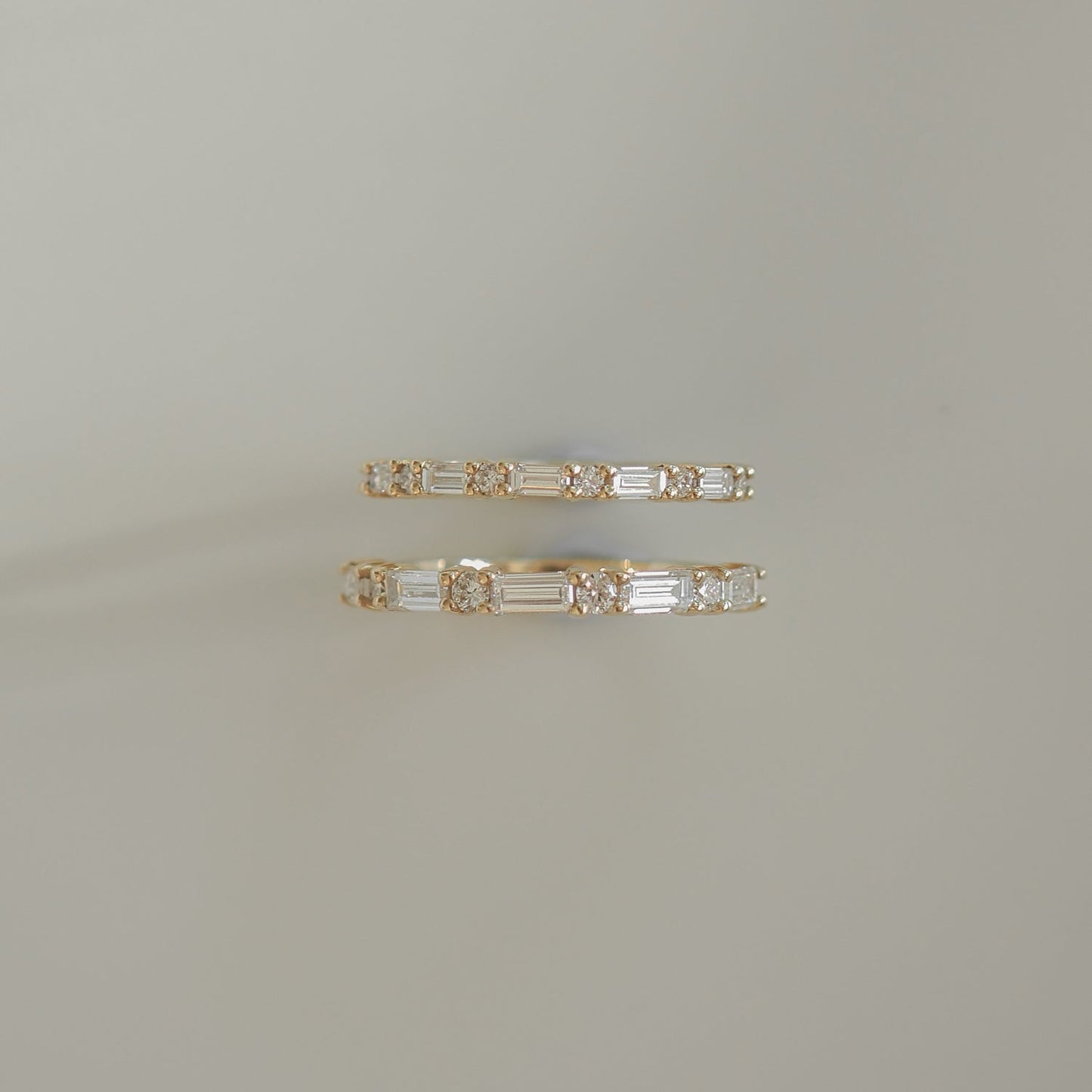 Gold hoop earrings with alternating baguette and round diamonds on a light grey background. Luxurious jewellery design.