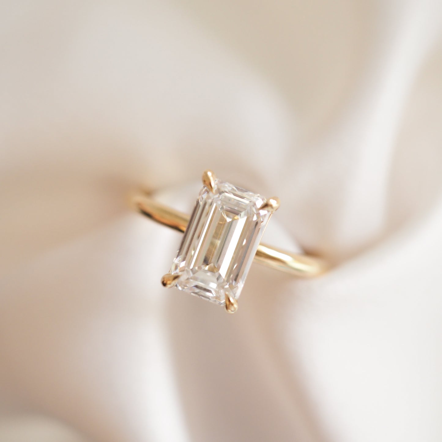 An emerald cut lab-grown diamond engagement ring in a gold setting, displayed on a satin fabric background.