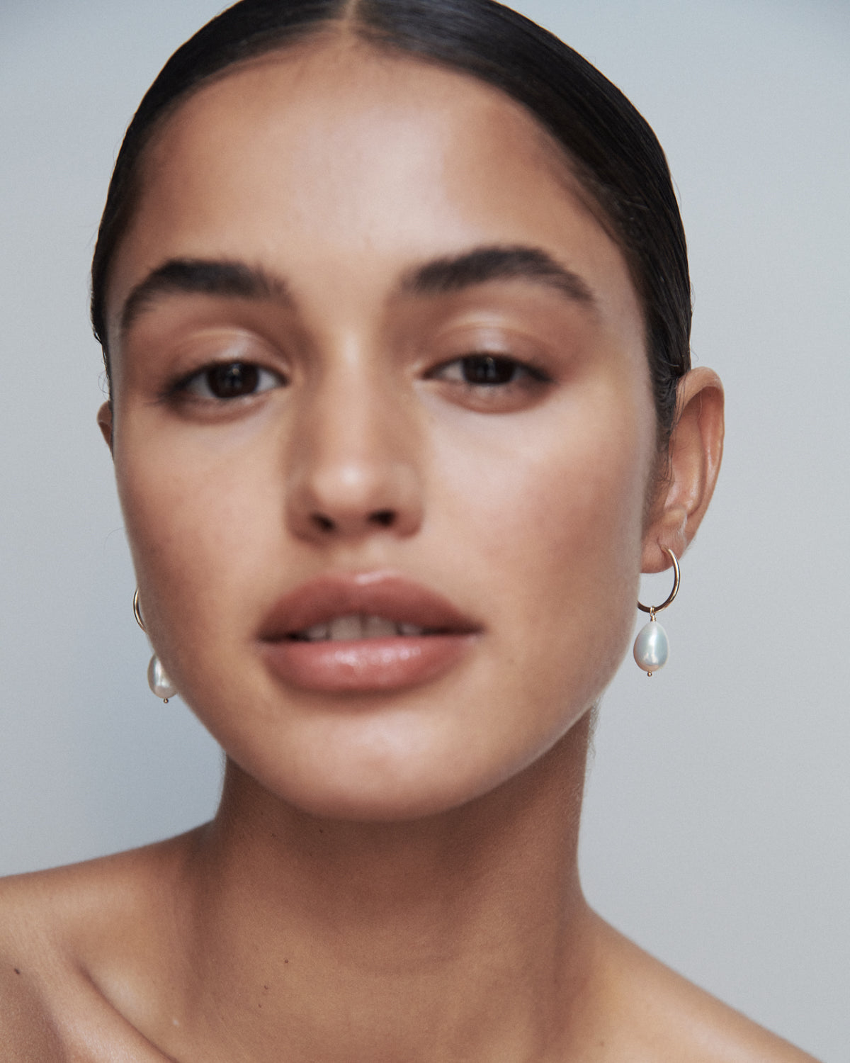 Woman wearing elegant pearl earrings, with sleek, pulled-back hair, and subtle makeup. Luxury jewellery fashion focus.