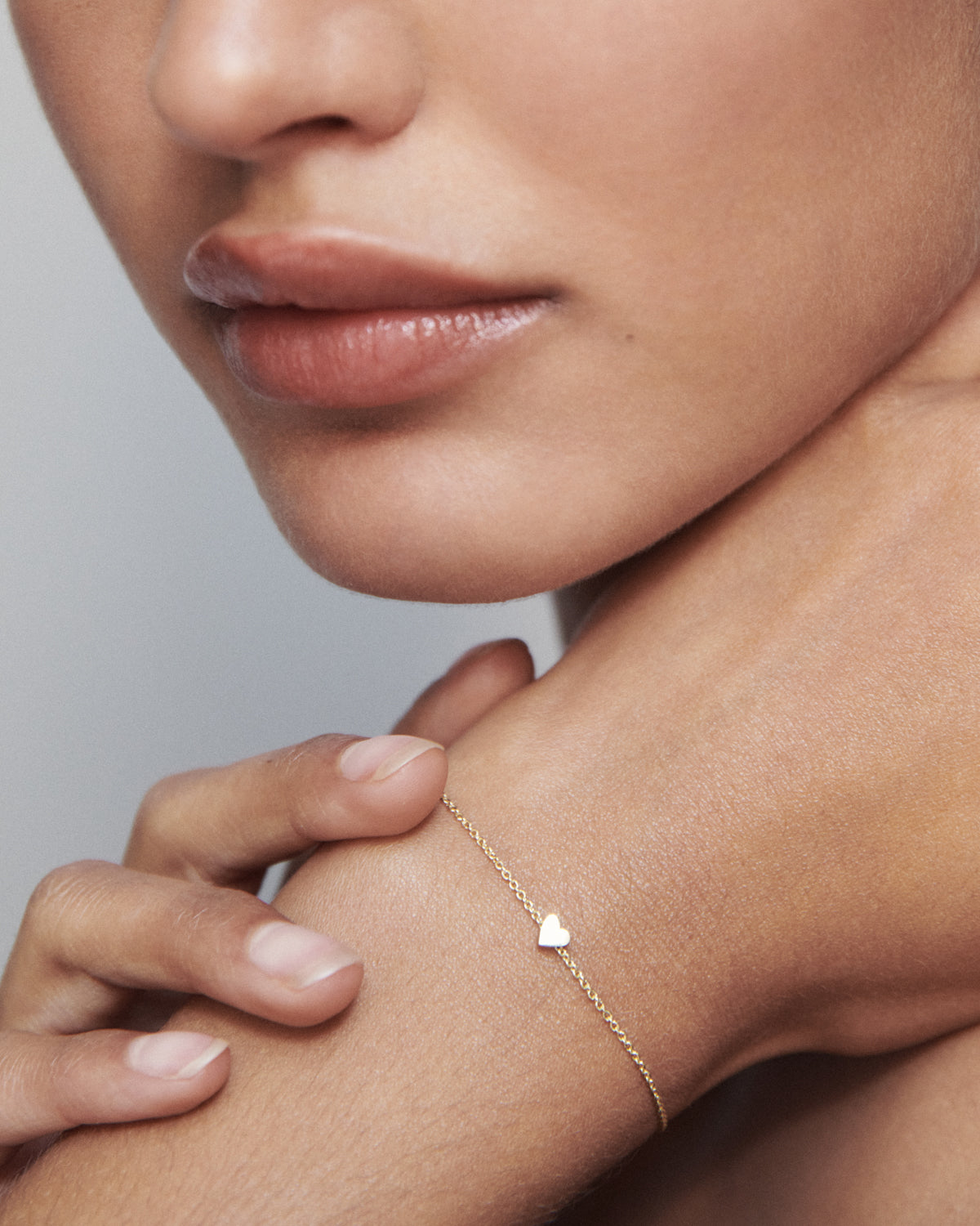 Close-up of a woman's neck and wrist, showcasing a delicate gold bracelet with a tiny heart charm, symbolising elegance and luxury jewellery.