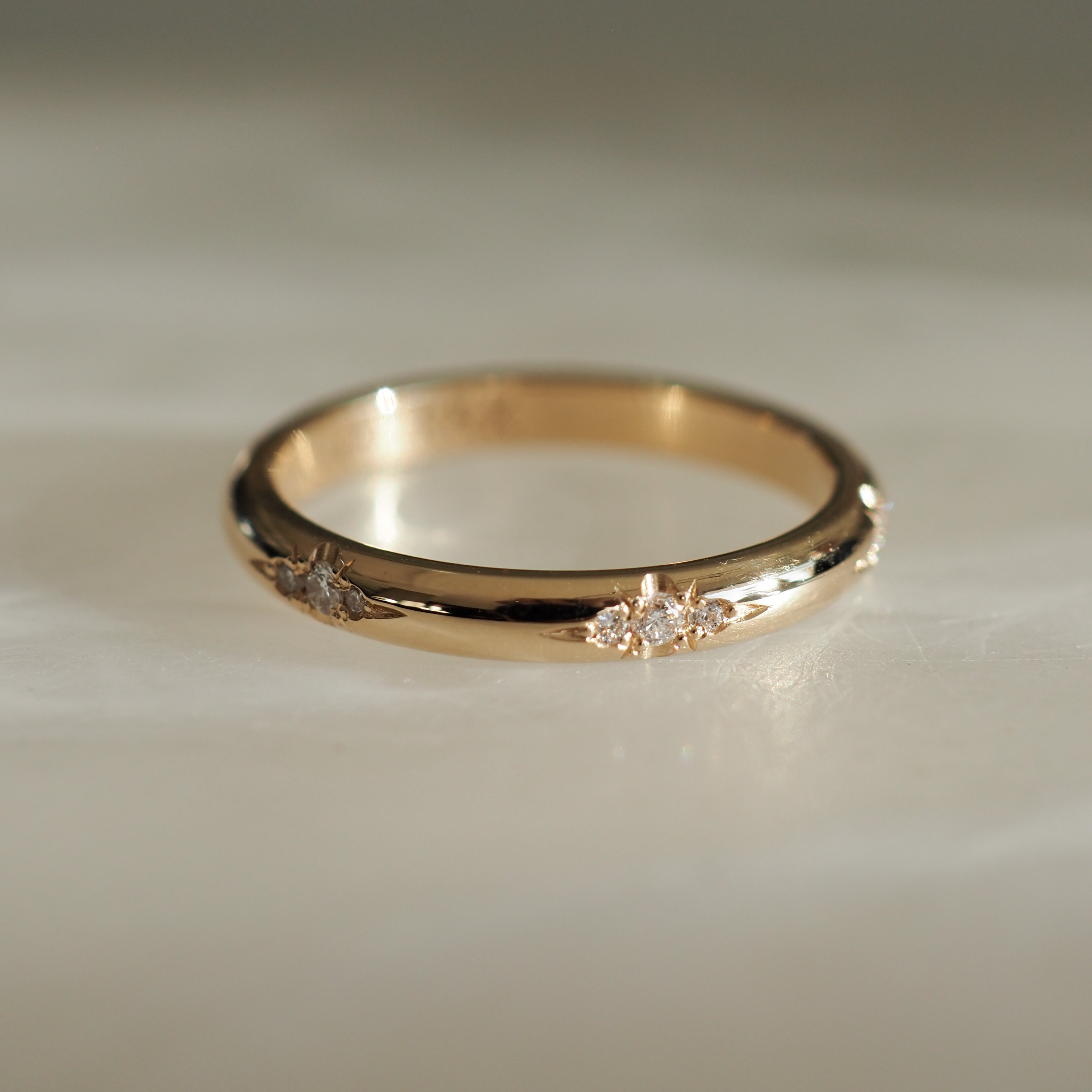 Elegant gold band with small, sparkling diamonds set in a delicate pattern, displayed on a soft, neutral surface. Luxurious jewellery design.