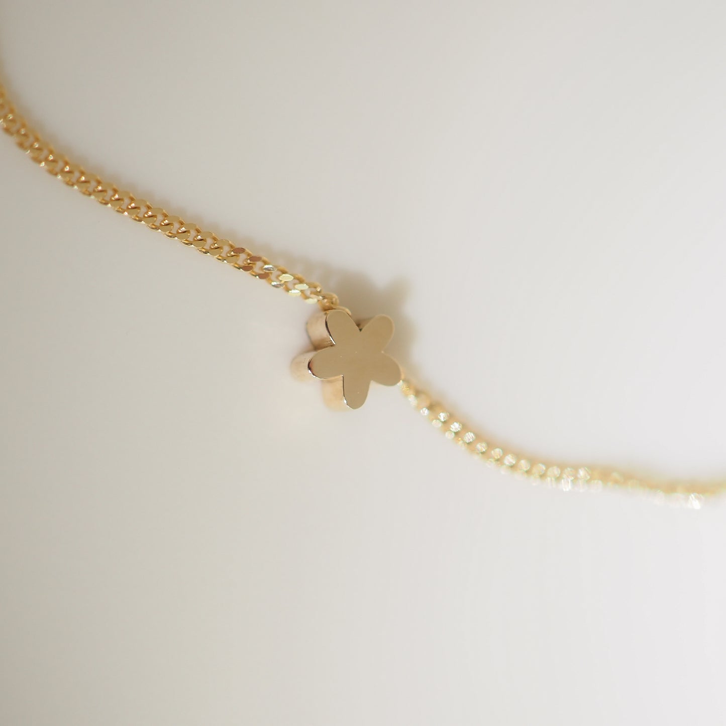 Gold necklace with a delicate flower-shaped pendant on a textured chain, set against a soft, neutral background.