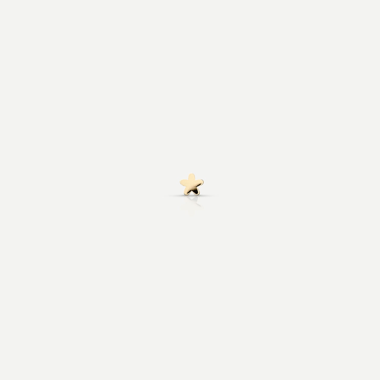Gold star-shaped stud earring on a light background; luxury jewellery minimalism.