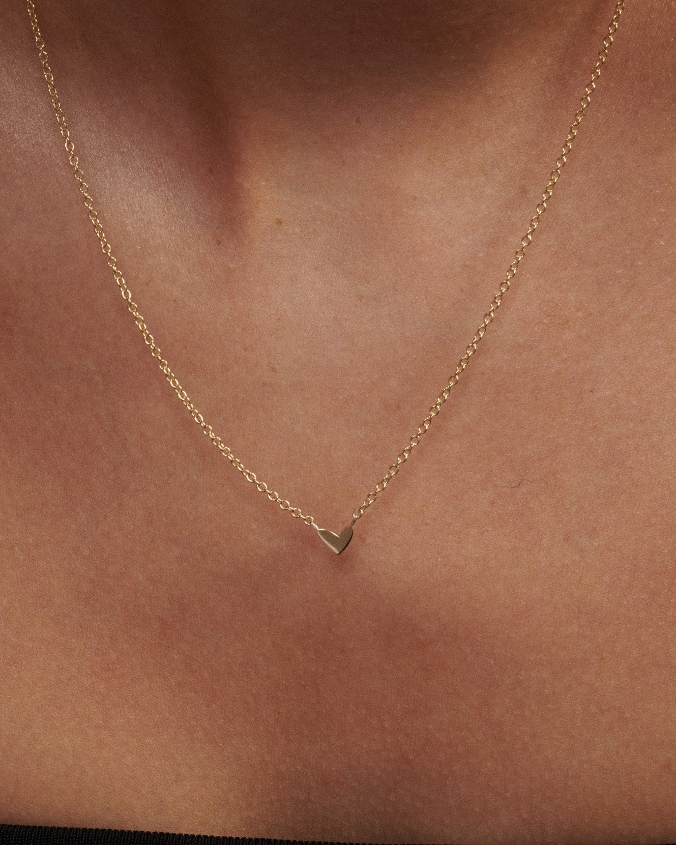 Gold necklace with a heart pendant on a person's neck