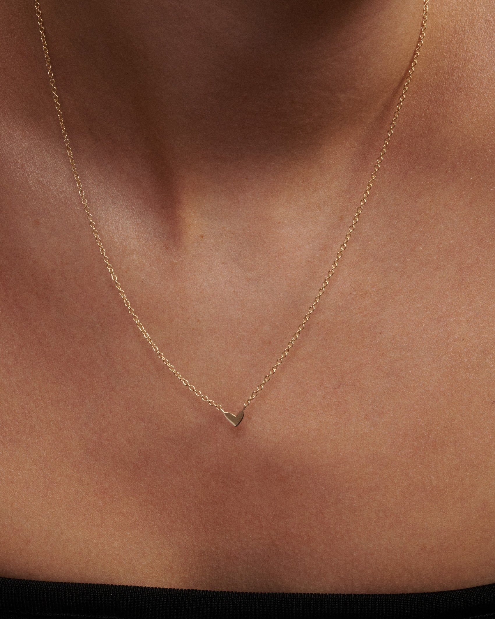 Gold necklace with a heart pendant on a person's neck