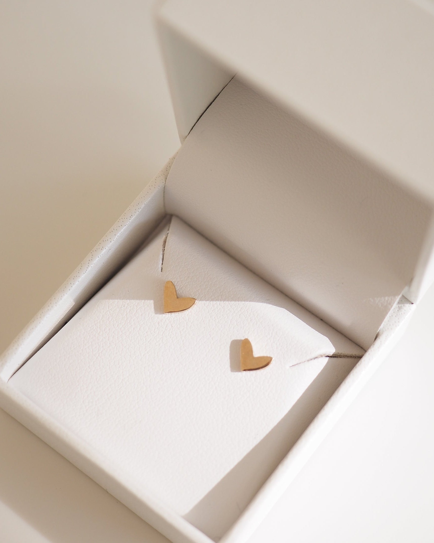 Gold heart earrings in a white jewellery box, showcased in soft lighting. Perfect for luxury, high-end jewellery lovers.