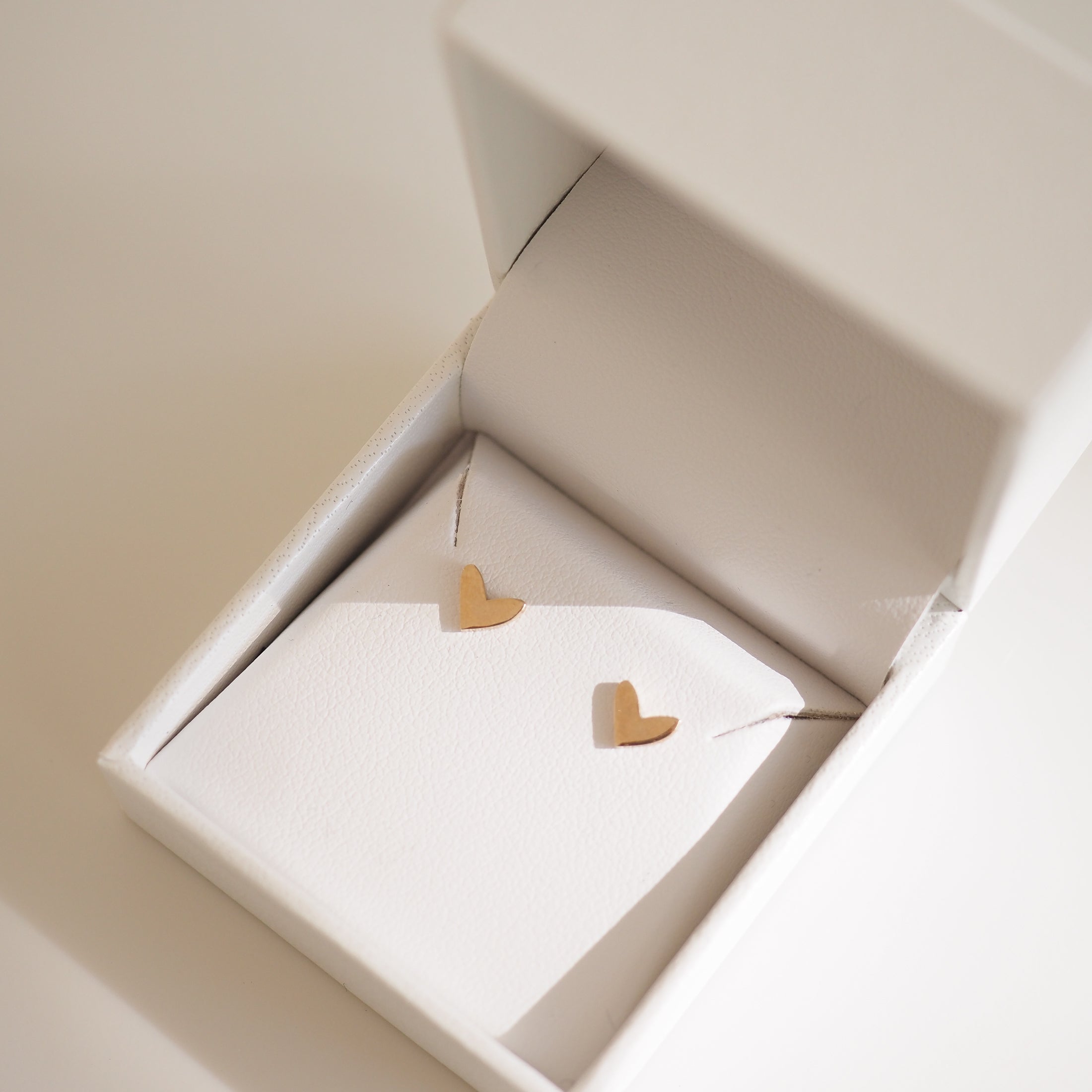 Gold heart earrings in a white jewellery box, showcased in soft lighting. Perfect for luxury, high-end jewellery lovers.