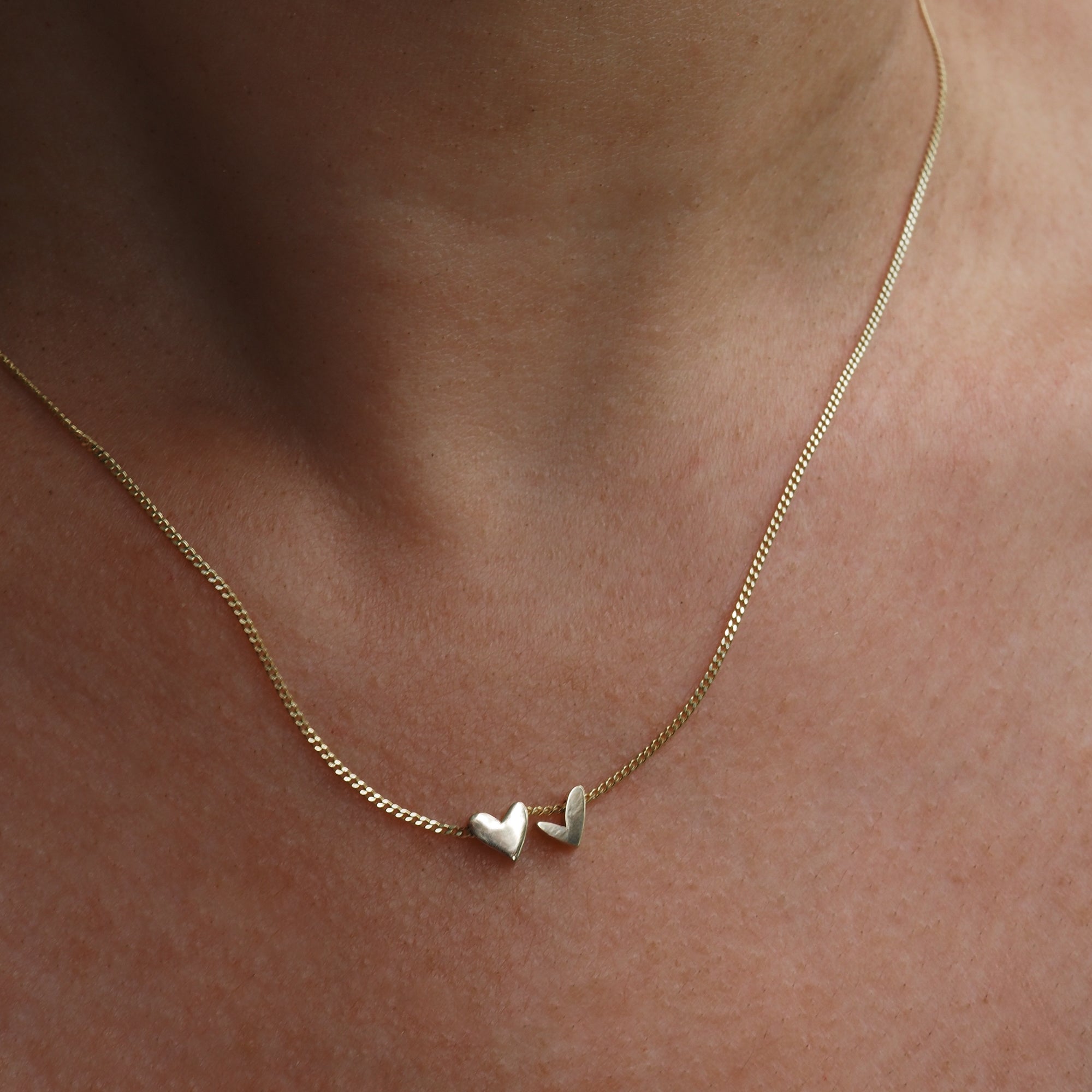 Gold necklace with two small heart pendants elegantly resting on a person's neck, showcasing minimalist luxury jewellery design.[text overlay: With two charms]
