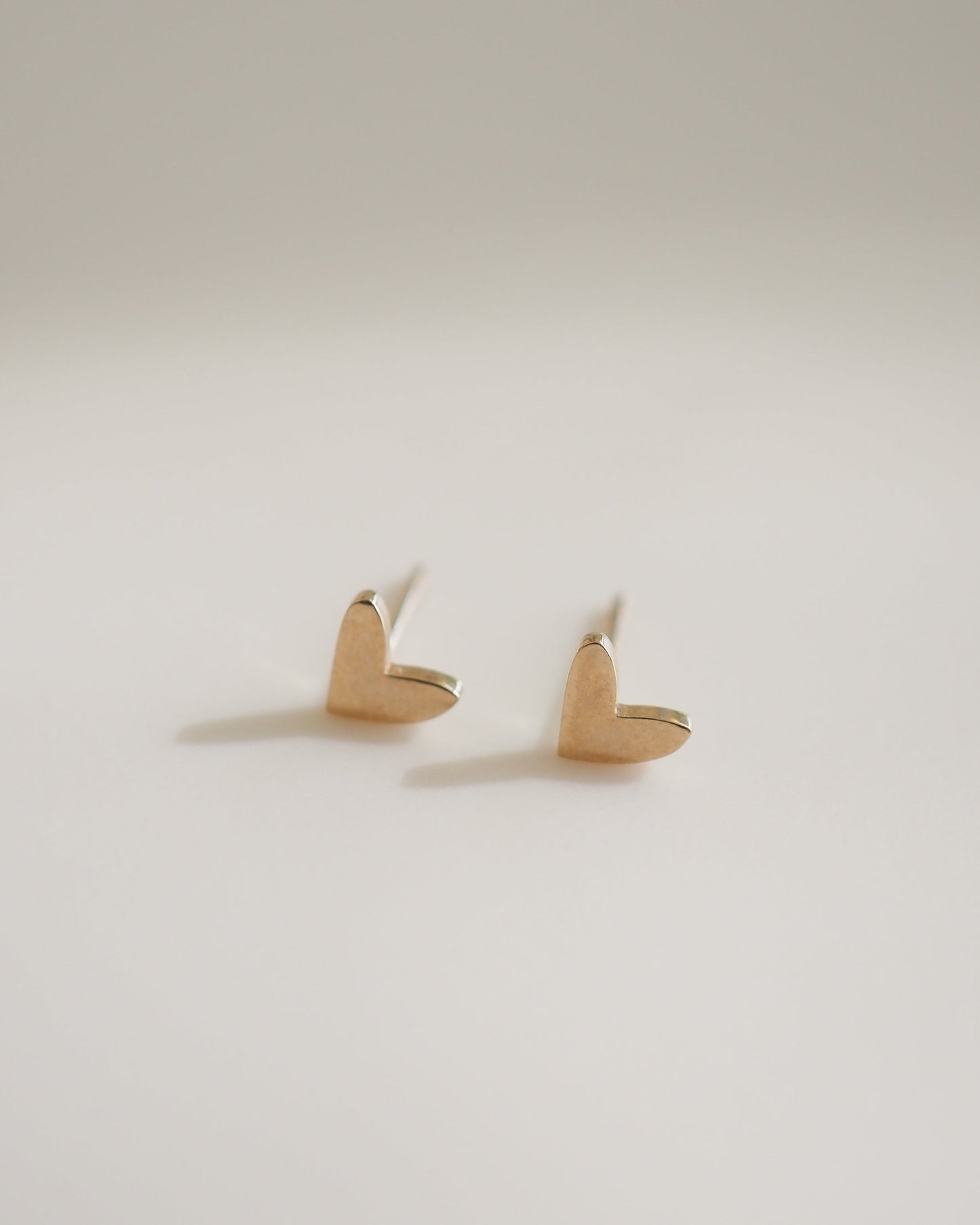 Elegant gold heart stud earrings on a plain background, showcasing minimalist luxury jewellery design.