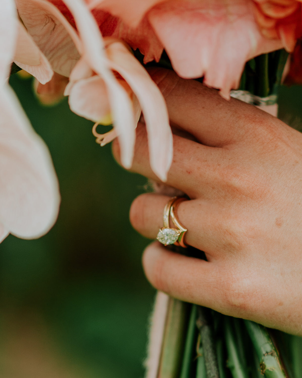 Hand holding a bouquet of pink flowers, wearing a luxurious diamond ring and gold band. Elegant jewellery with floral background.