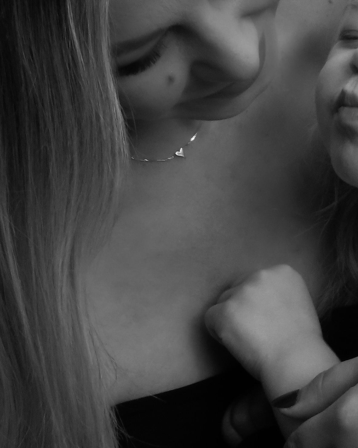 Black and white photo of a woman wearing a delicate heart necklace, with a child holding her arm affectionately.