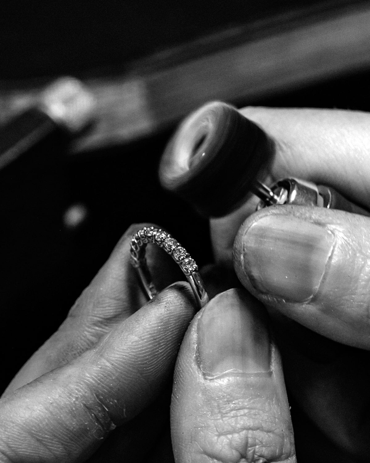Close-up of hands holding a diamond ring against a dark background