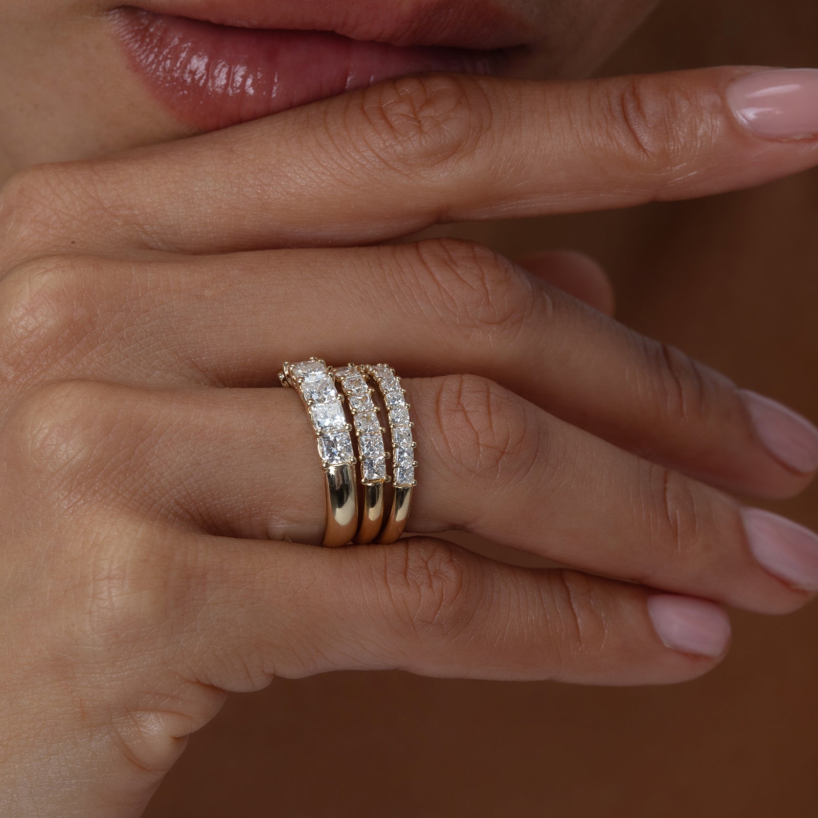 Close-up of a hand wearing three gold and diamond rings on a neutral background
