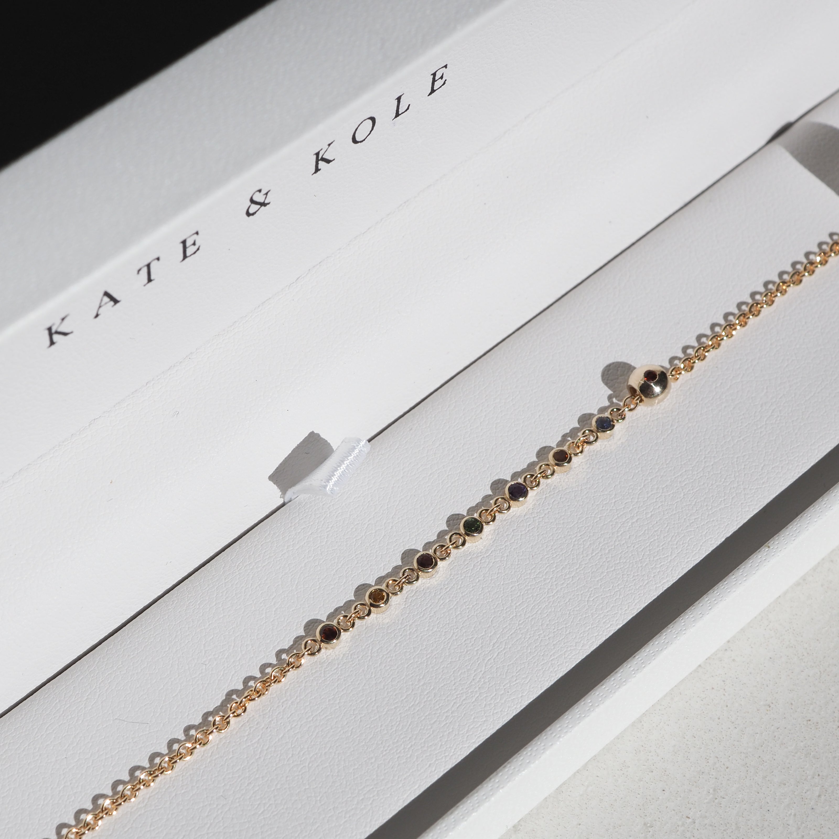 Elegant gold bracelet adorned with delicate gemstones in a Kate & Kole jewellery box, showcasing luxury and craftsmanship.[text overlay: Custom bracelet with Tiny Birthstone Charm added] [text colour: #000000]
