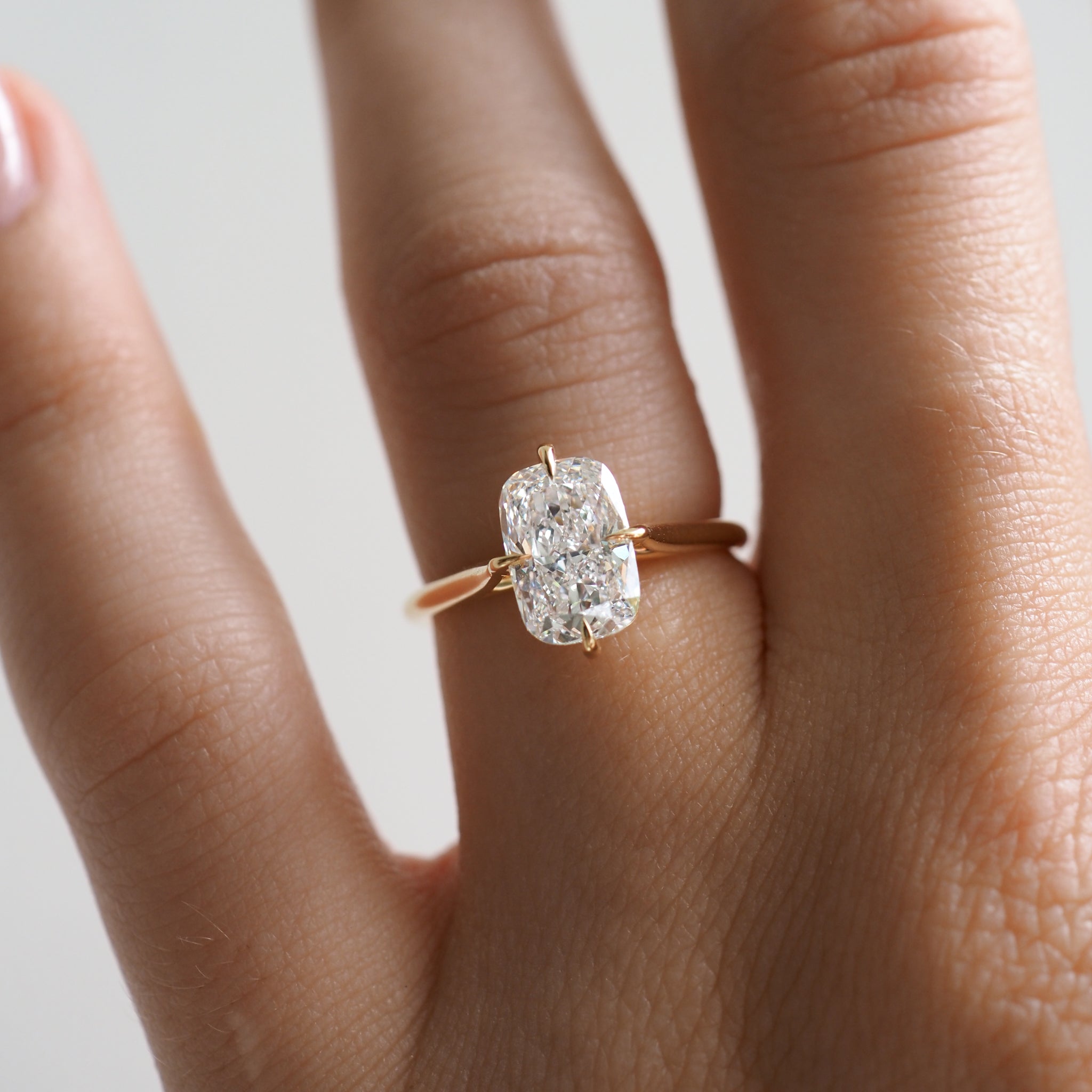 Close-up of a hand wearing a gold ring with a large cushion-cut diamond, symbolising luxury jewellery.