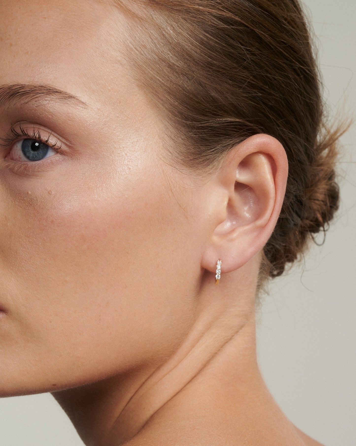 Close-up of a woman's ear wearing a diamond earring against a neutral background