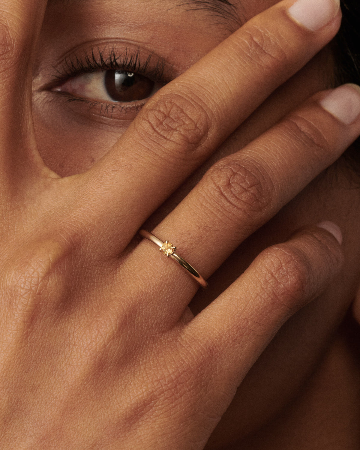 Woman wear a citrine yellow gold birthstone ring up to her eye [text overlay: Citrine Birthstone Ring]