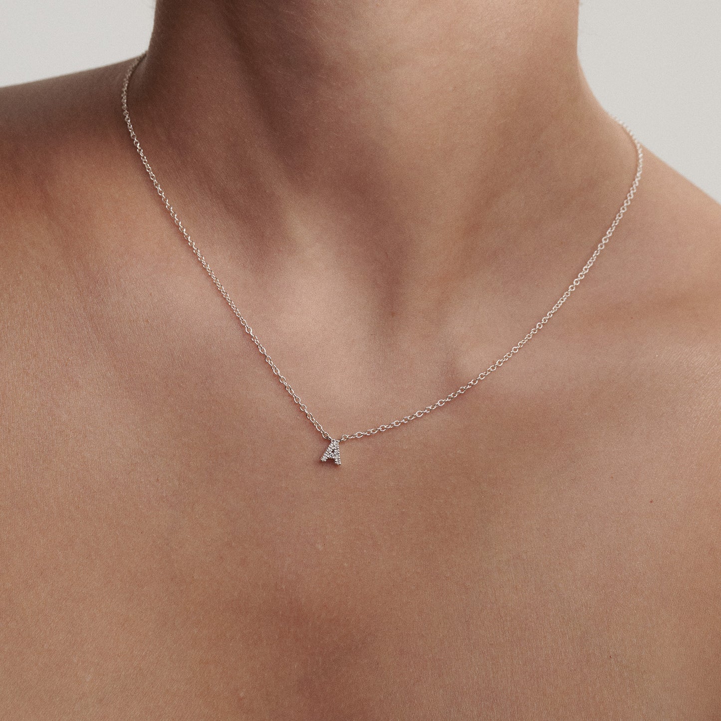 Silver necklace with a small diamond letter pendant on a person's neck against a neutral background