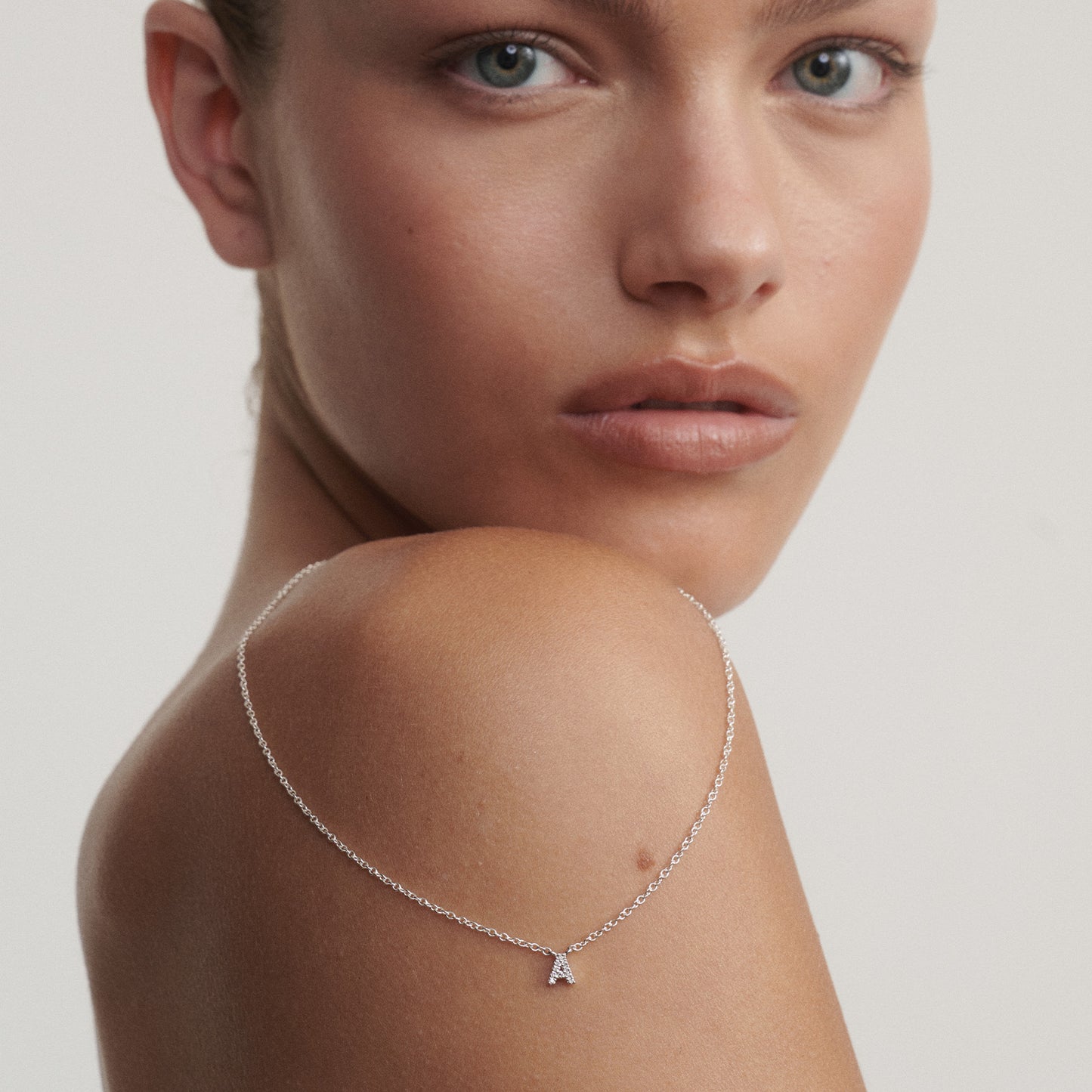 Woman wearing a delicate silver necklace with a small pendant on a neutral background