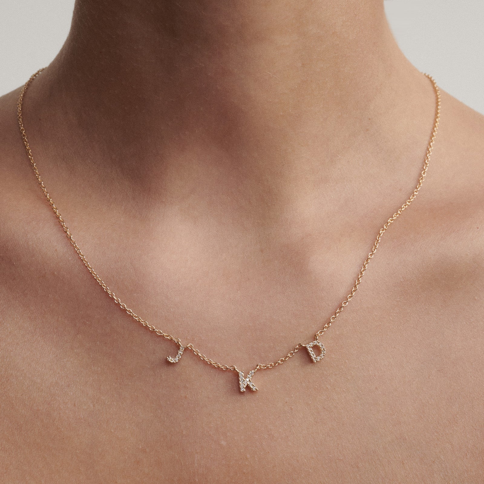 Yellow gold necklace with letter charms on a person's neck against a neutral background. The perfect gift for a mum or friend.