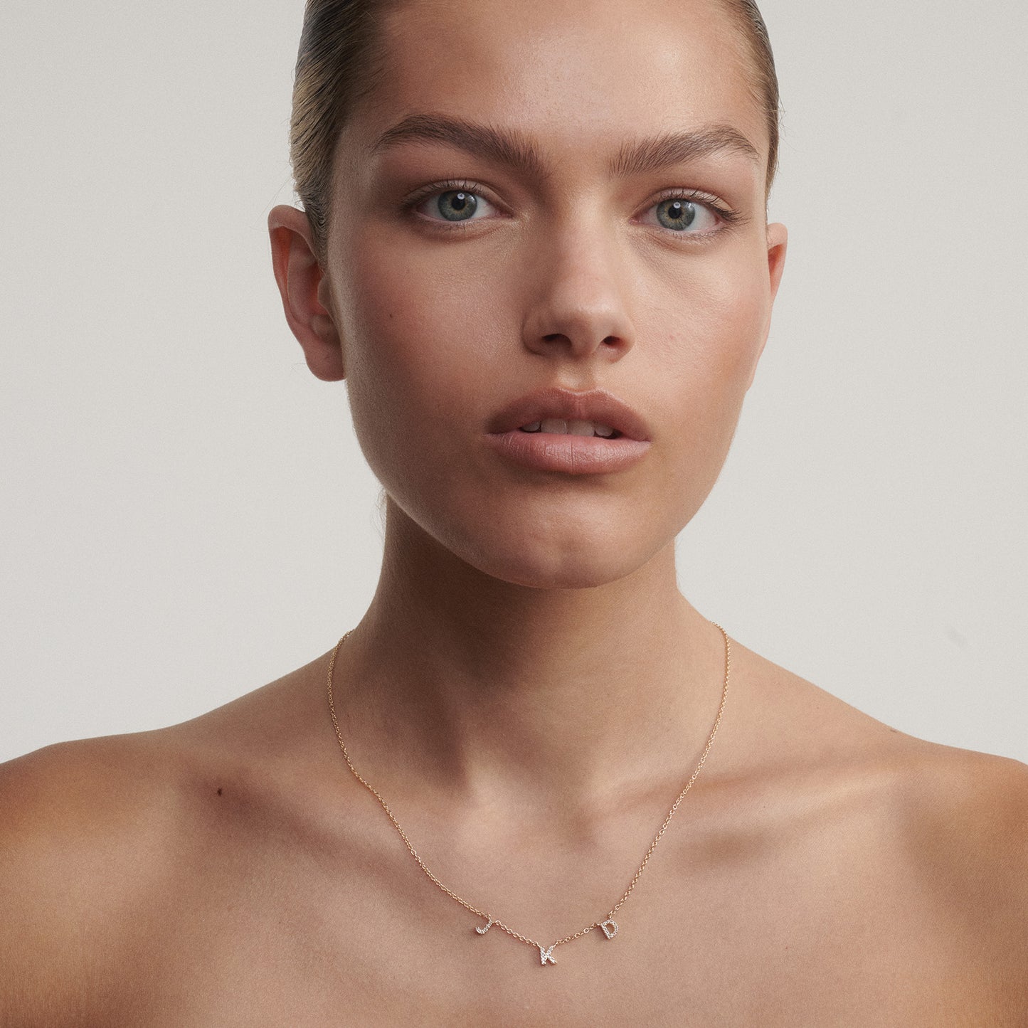Woman wearing a delicate three letter necklace with a plain background