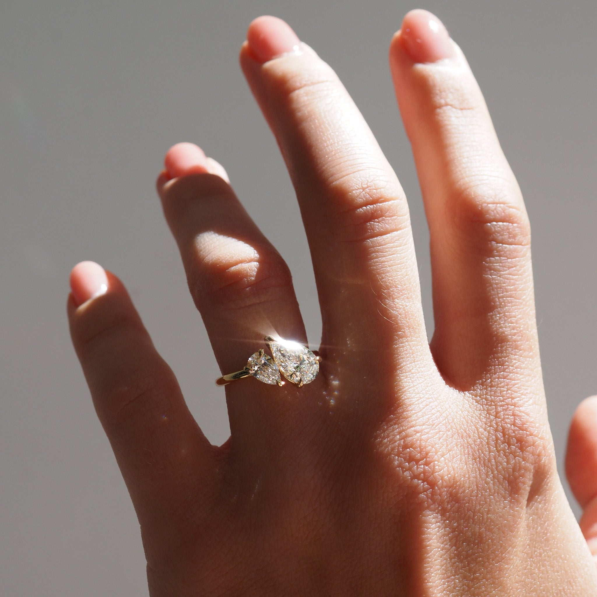 Hand model wearing a duet pear diamond ring with a neutral background