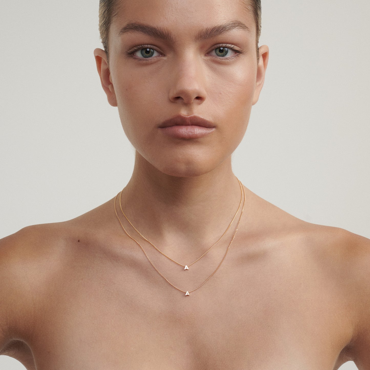 Woman wearing a delicate gold necklace with a triangle pendant on a neutral background

[text overlay: 40cm length (top) and 45cm length (Bottom)]