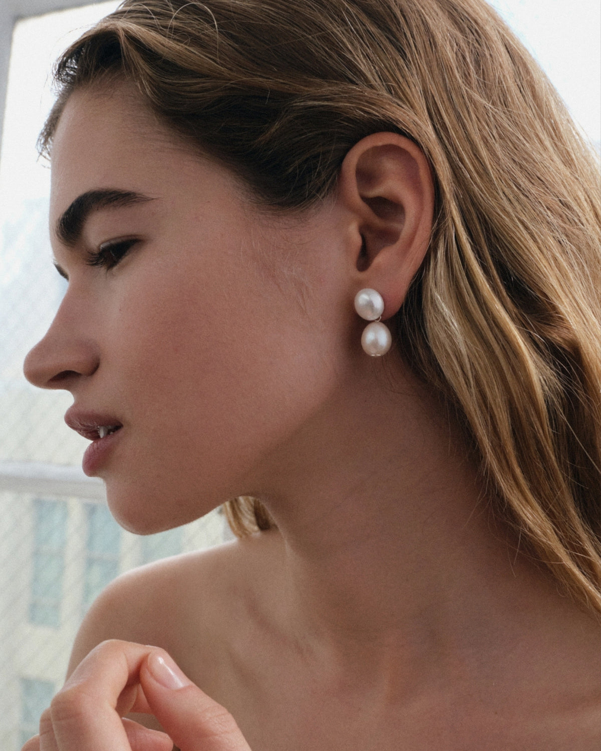 Close-up of a woman wearing pearl earrings with a display of heart-shaped engravable pendants on a white background.
