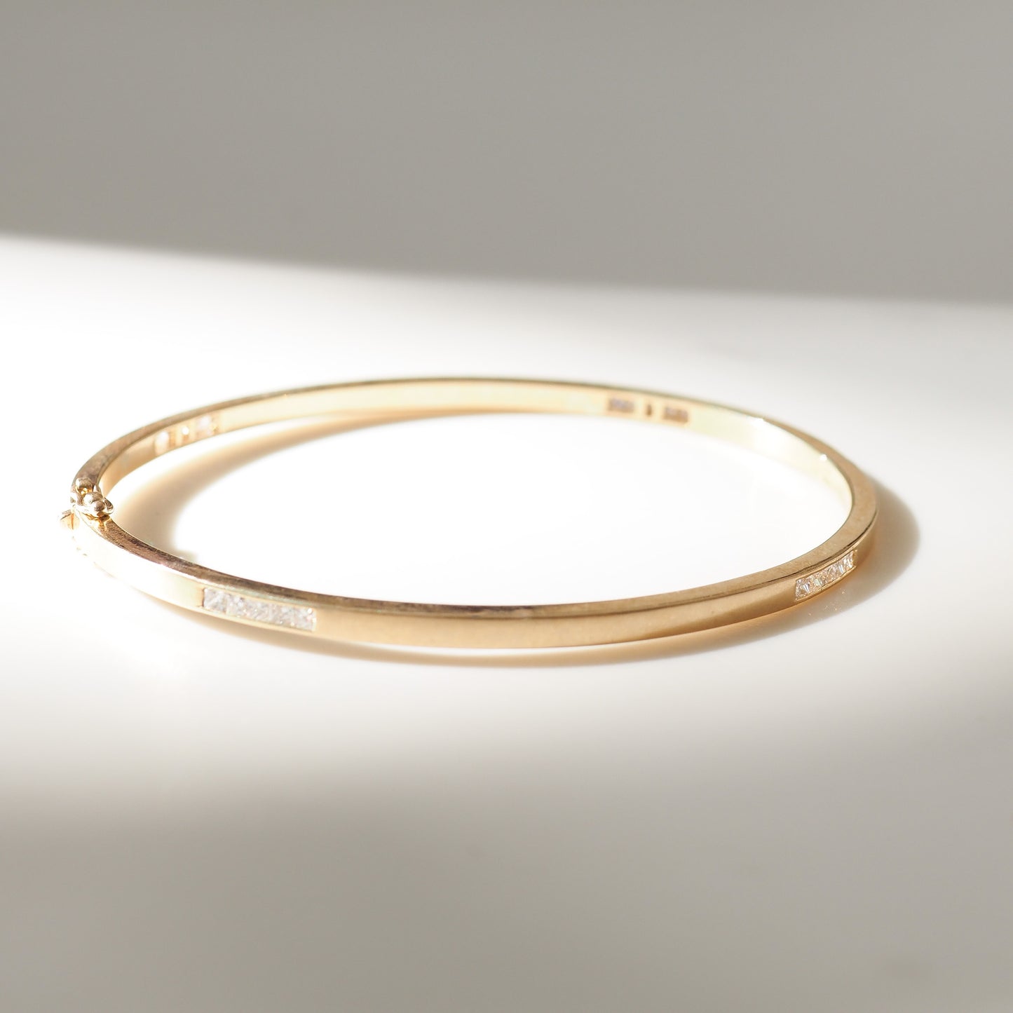 Gold bracelet with embedded diamonds on a light gray background