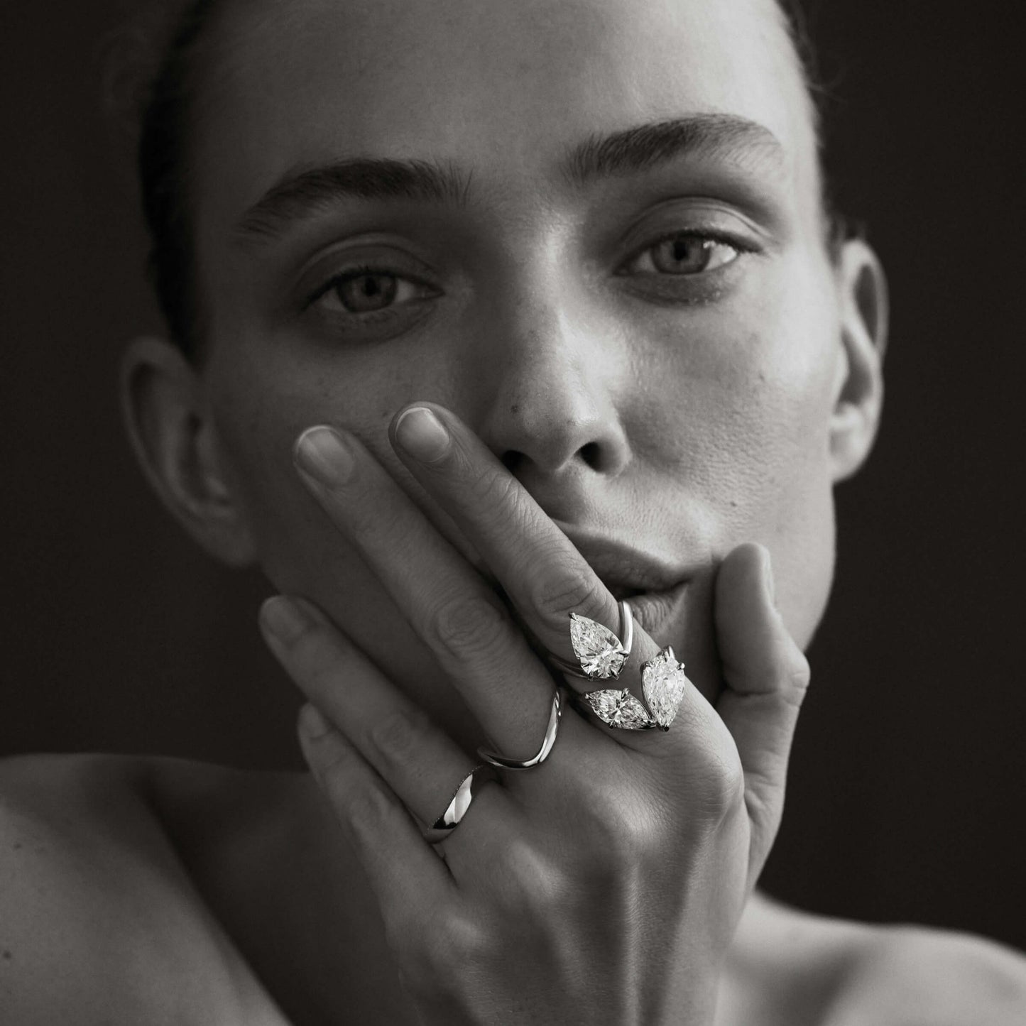 Black and white portrait of a person wearing diamond jewelry with a dark background
[text overlay: Model wears (from left to right) Piece 6, Piece 9, Piece 4, Piece 3]