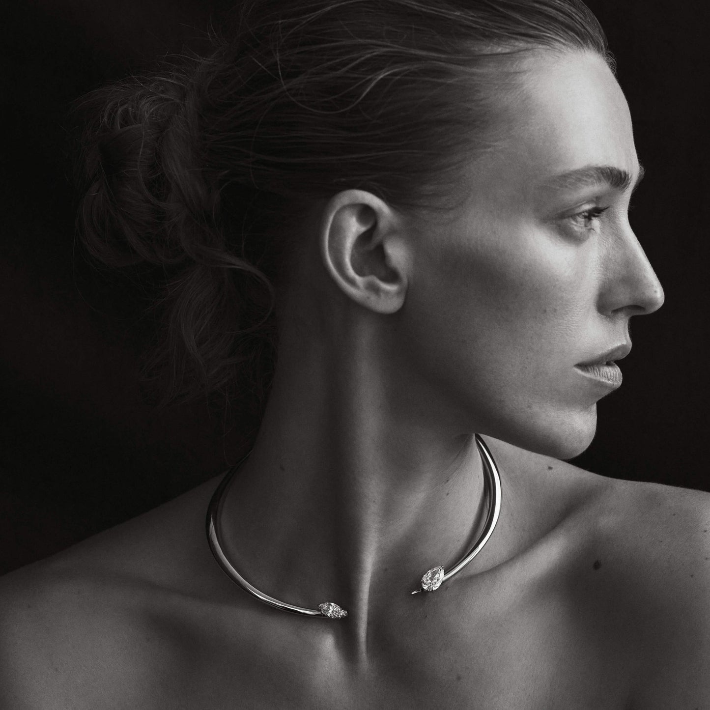 Black and white portrait of a woman wearing a necklace with a dark background