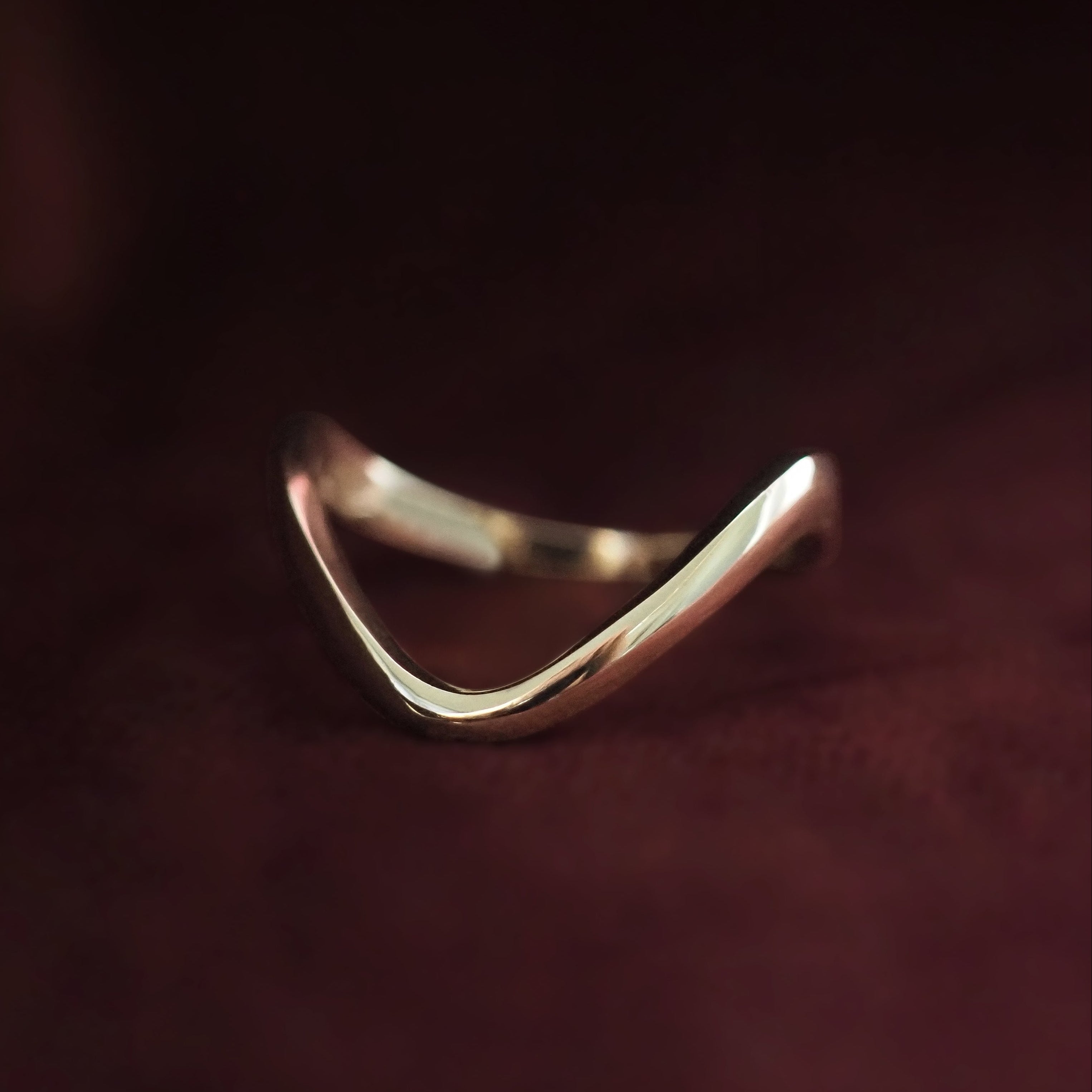 Gold ring with a wavy design on a dark background