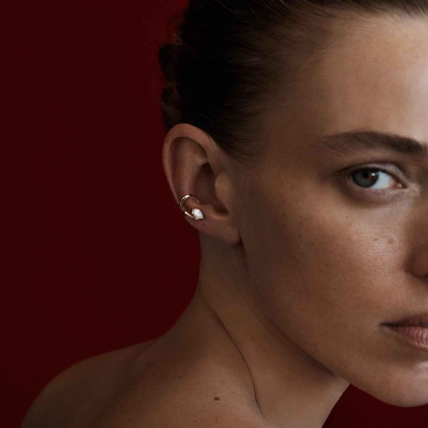 Close-up of a woman's ear with an earring against a red background
