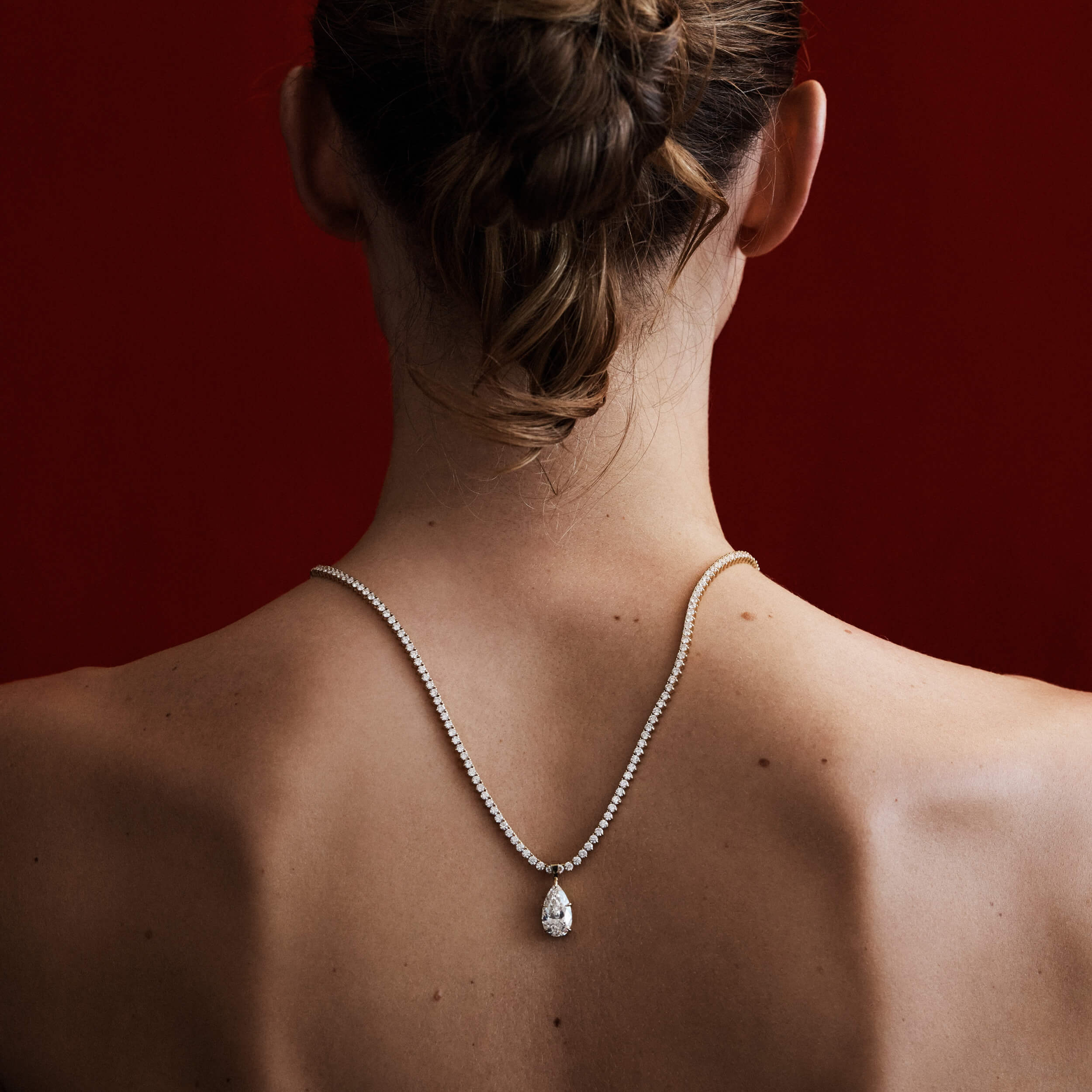Person wearing a necklace with a teardrop pendant on a red background