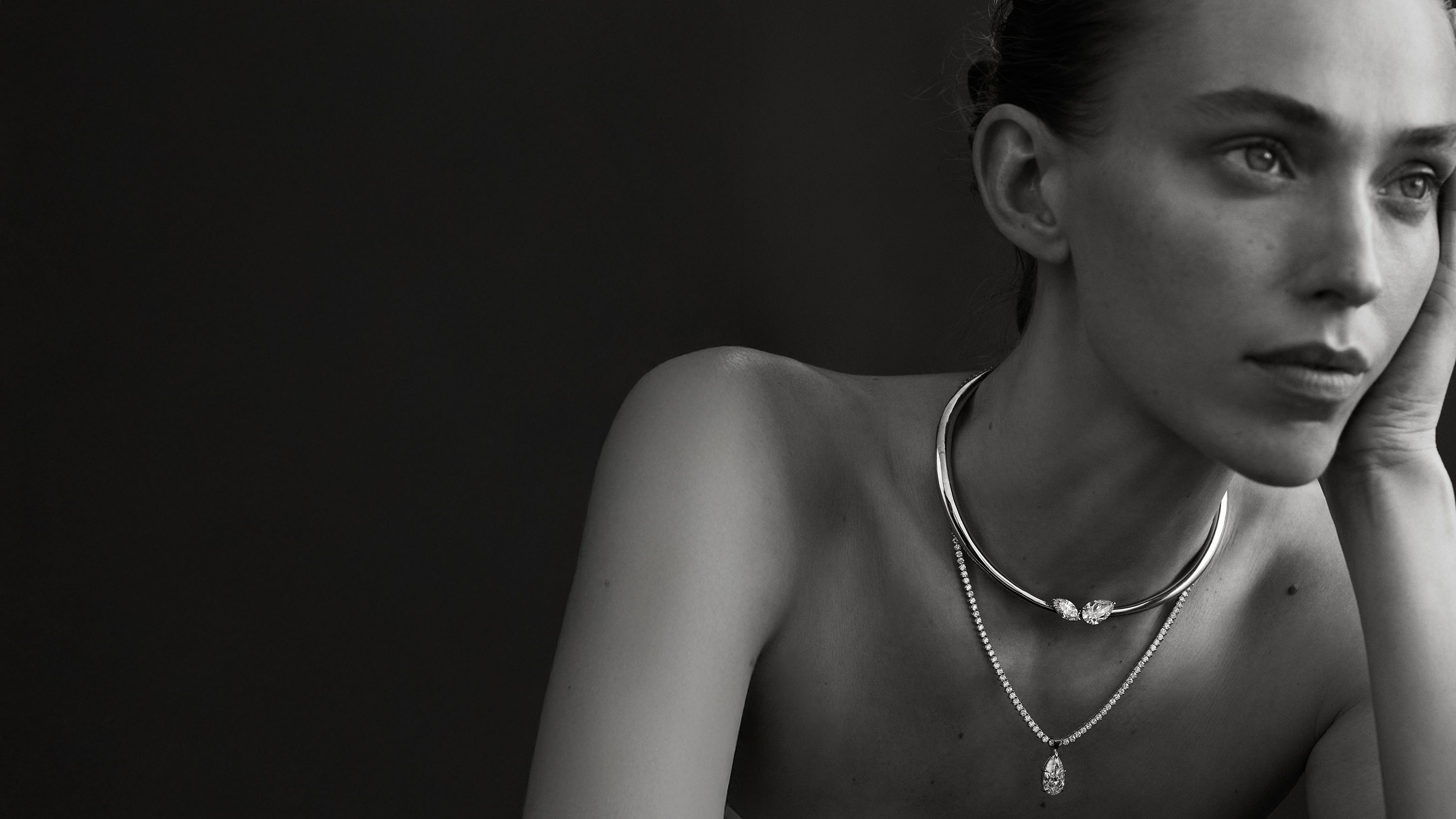 Black and white portrait of a woman wearing necklaces against a dark background
