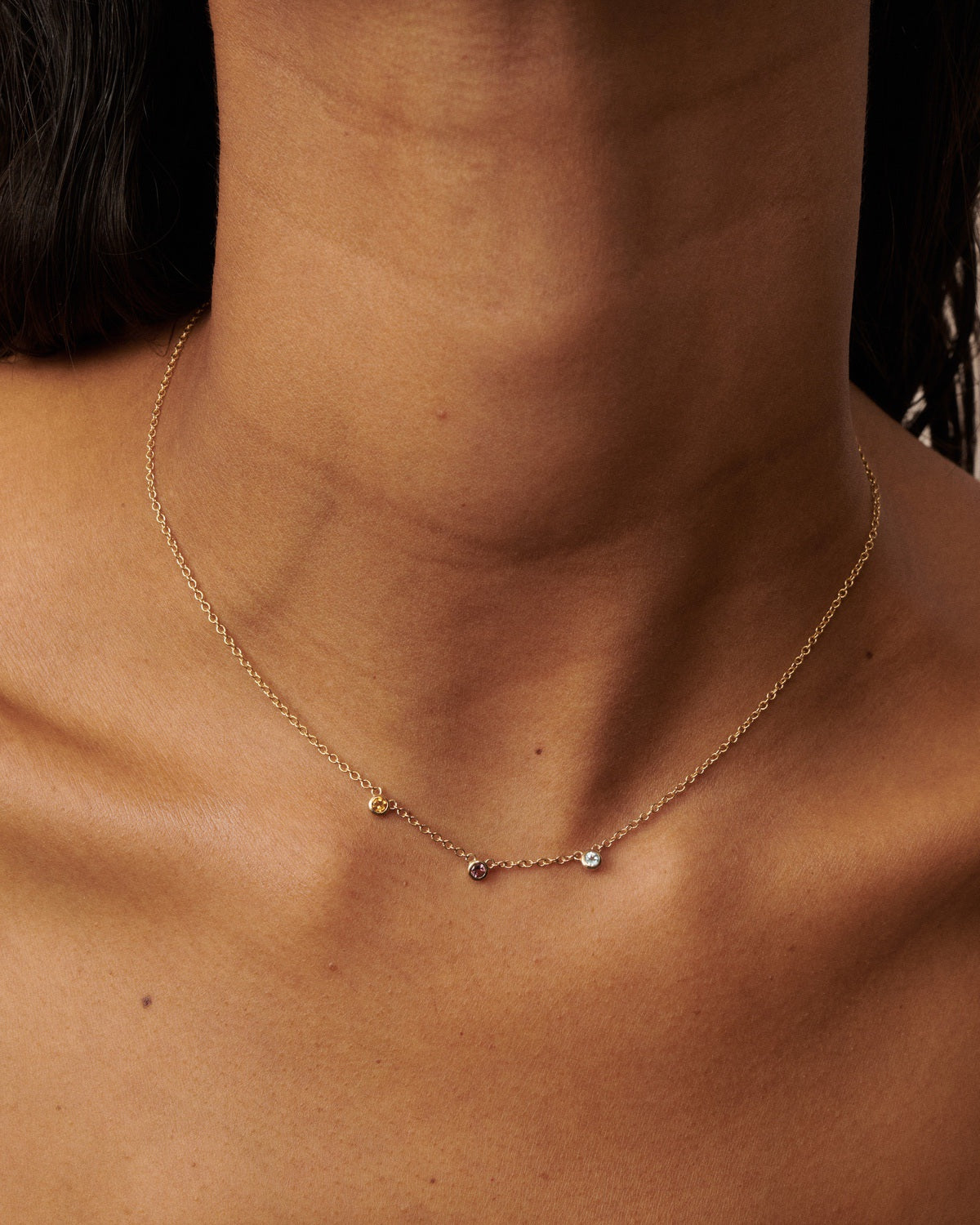 A delicate gold chain necklace with three small, individually colored gemstone beads (citrine, pink tourmaline, and diamond) worn on a model's neck.