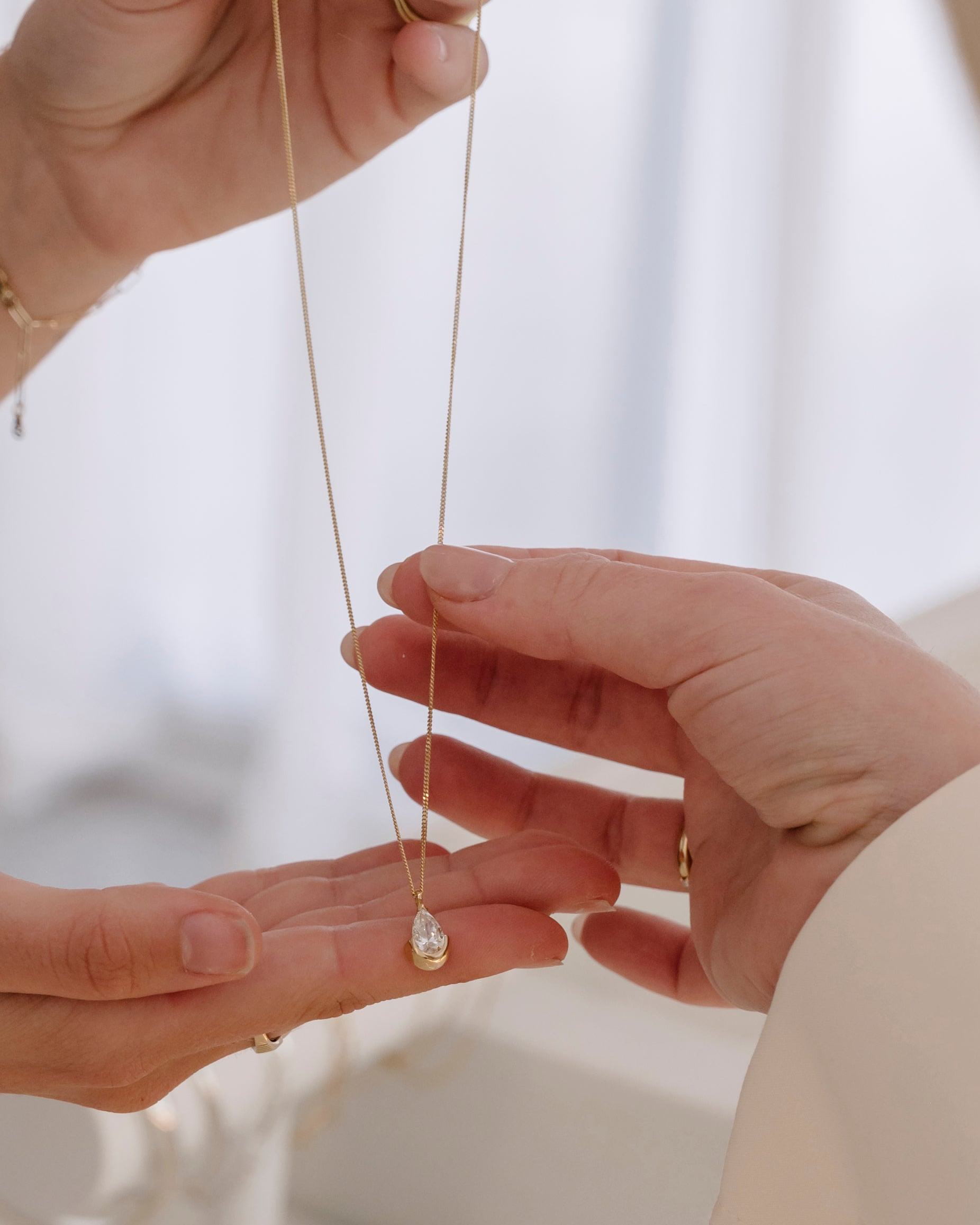 Two hands holding a delicate necklace with a blurred background