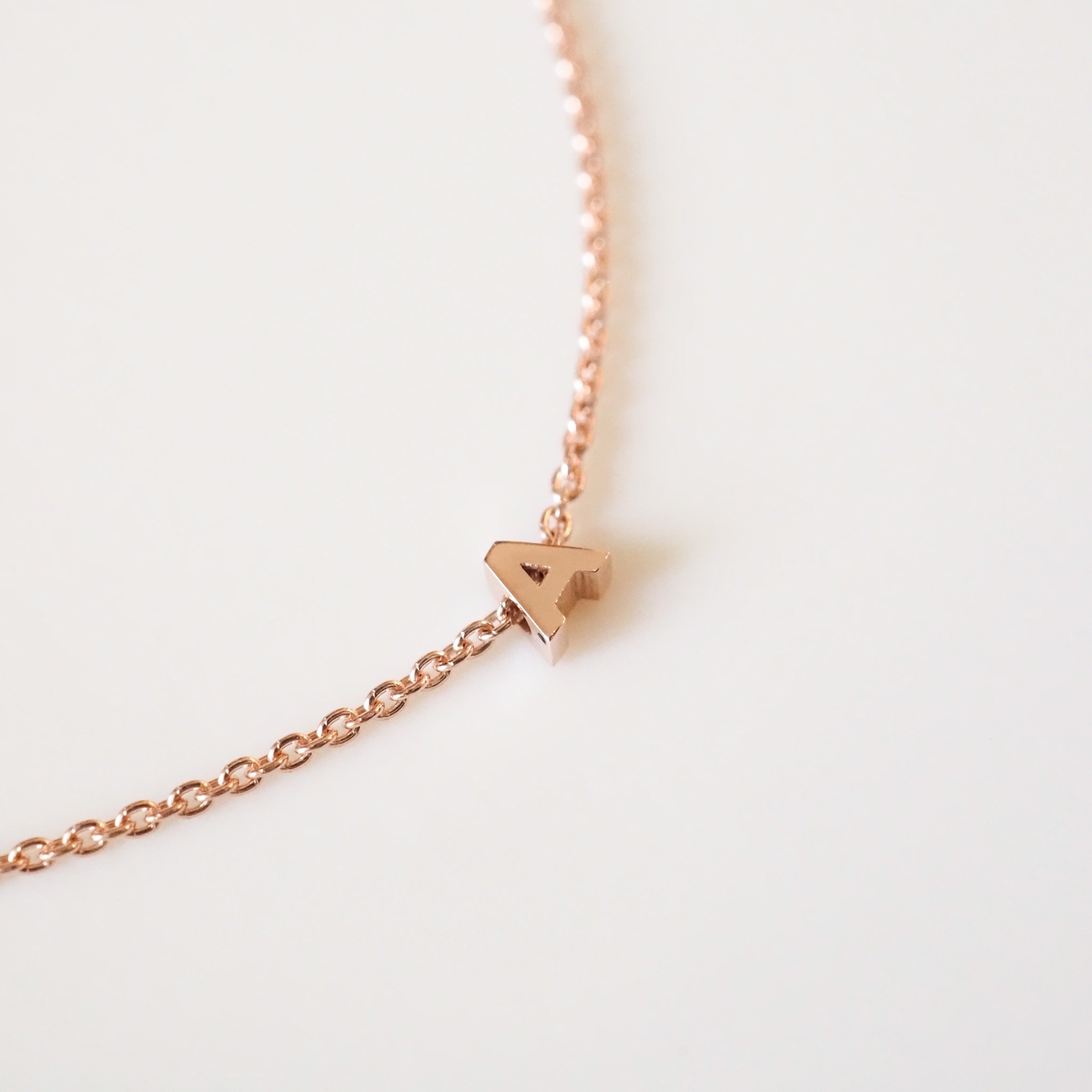Rose gold necklace with a small triangle pendant on a light gray background