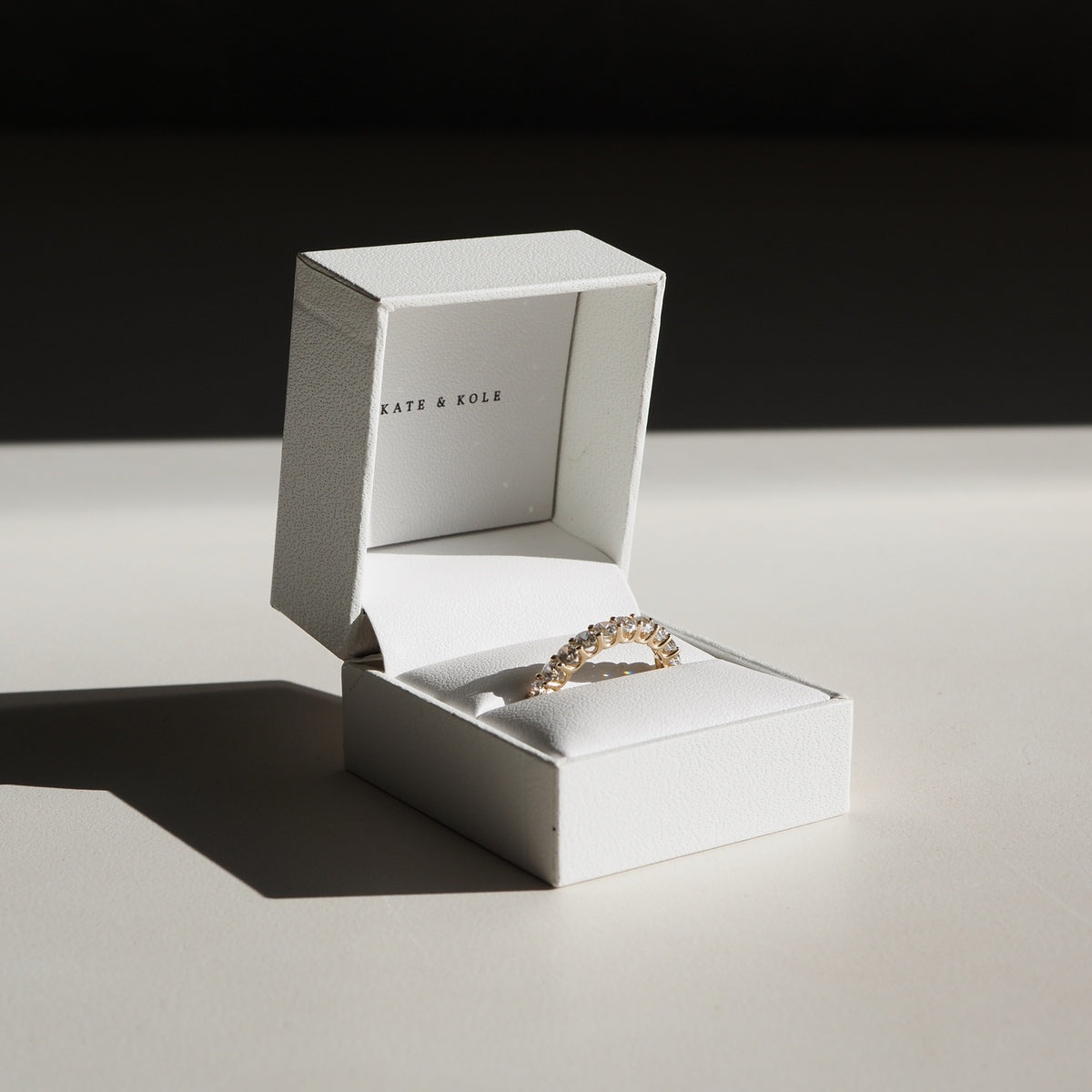 A diamond band sits on a table in a ring box.