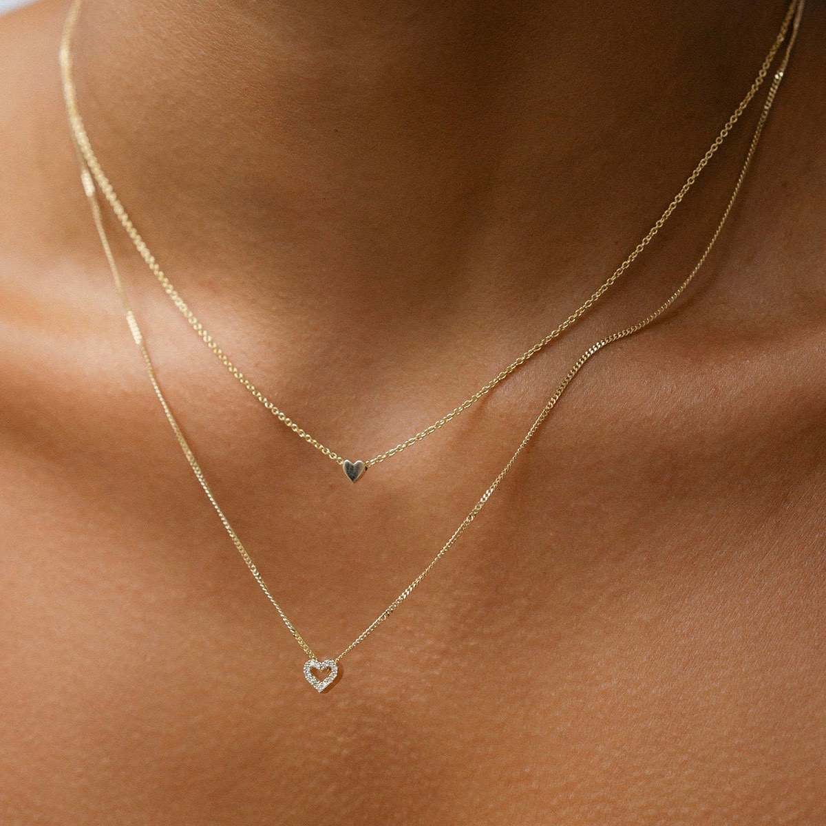 Model wears our beautiful Diamond Heart Charm Necklace in 9ct yellow gold, with a 45cm diamond curb chain layered with our 40cm solid gold Tiny Letter Necklace. [text overlay: Tiny Heart Necklace (top) and Diamond Heart Charm Necklace (bottom)]
