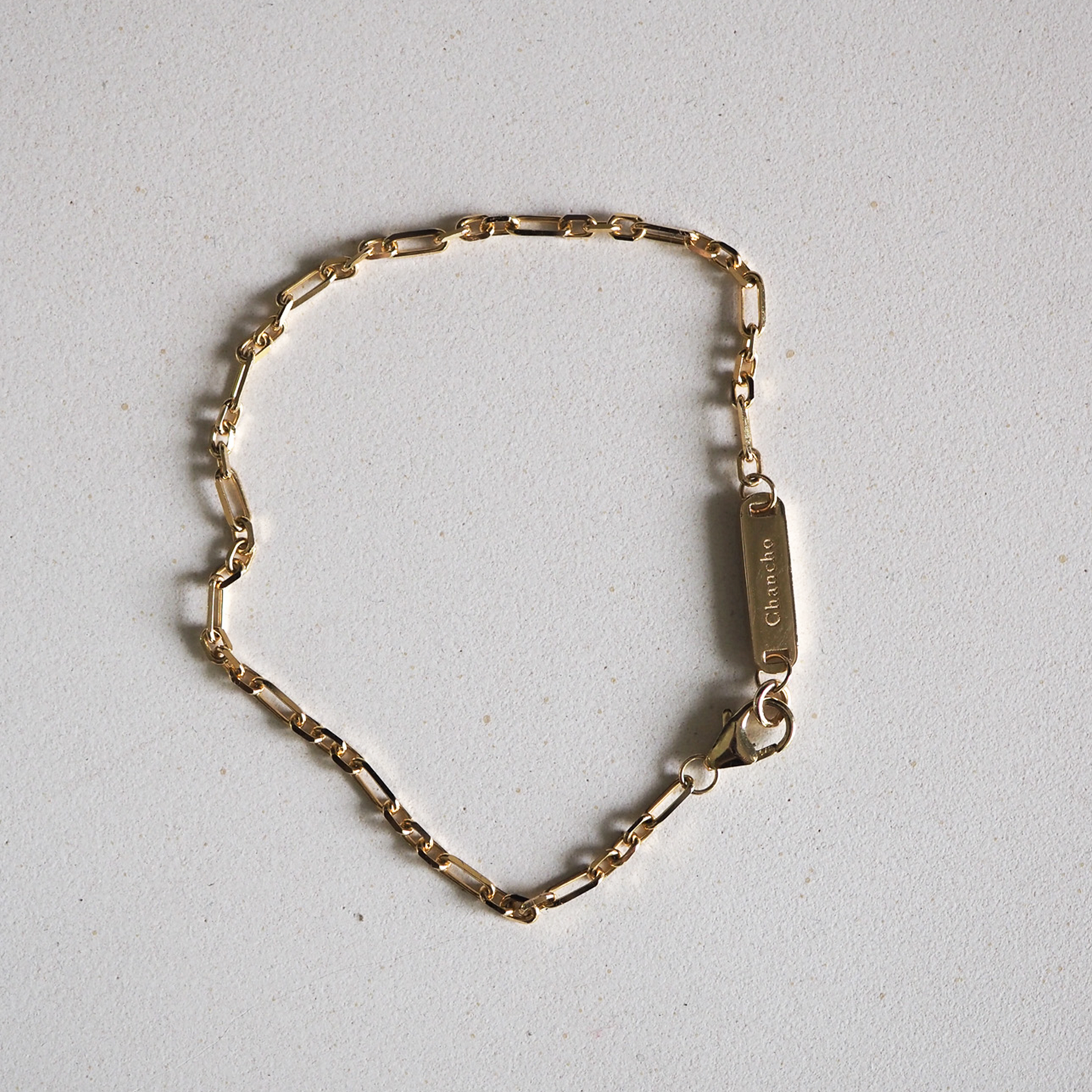 Gold link bracelet with an engraved rectangular pendant on a light grey background. Luxury jewellery, elegant design.
