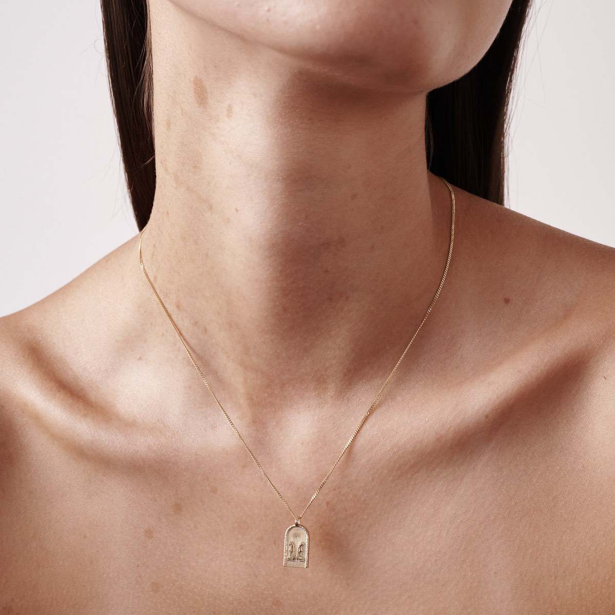 Gold necklace with a small, arch-shaped pendant on a woman's neck, showcasing minimalist fine jewellery.